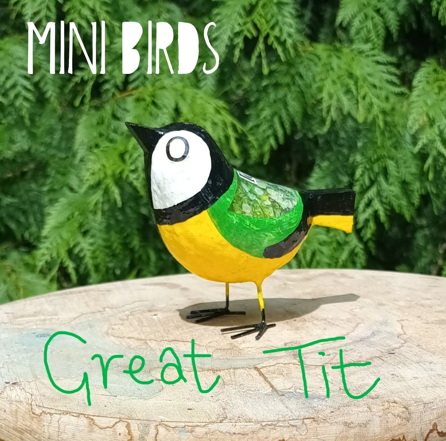 A small Posh Paper Mache mixed media Great Tit bird sculpture standing on a wooden plinth against a backdrop of pine trees, photographed in the artists garden.