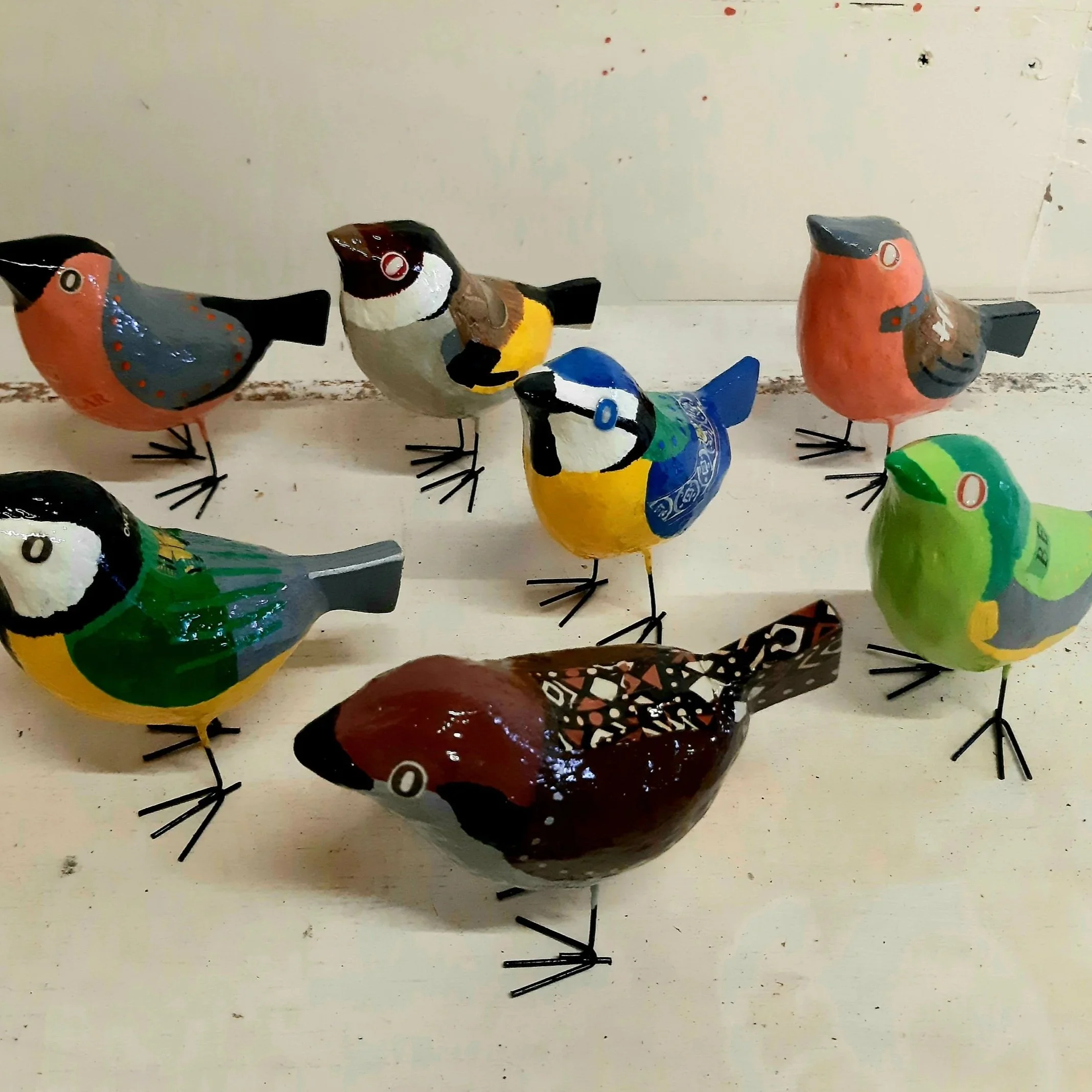 Colorful decorative bird figurines arranged on a white surface with a plain background.