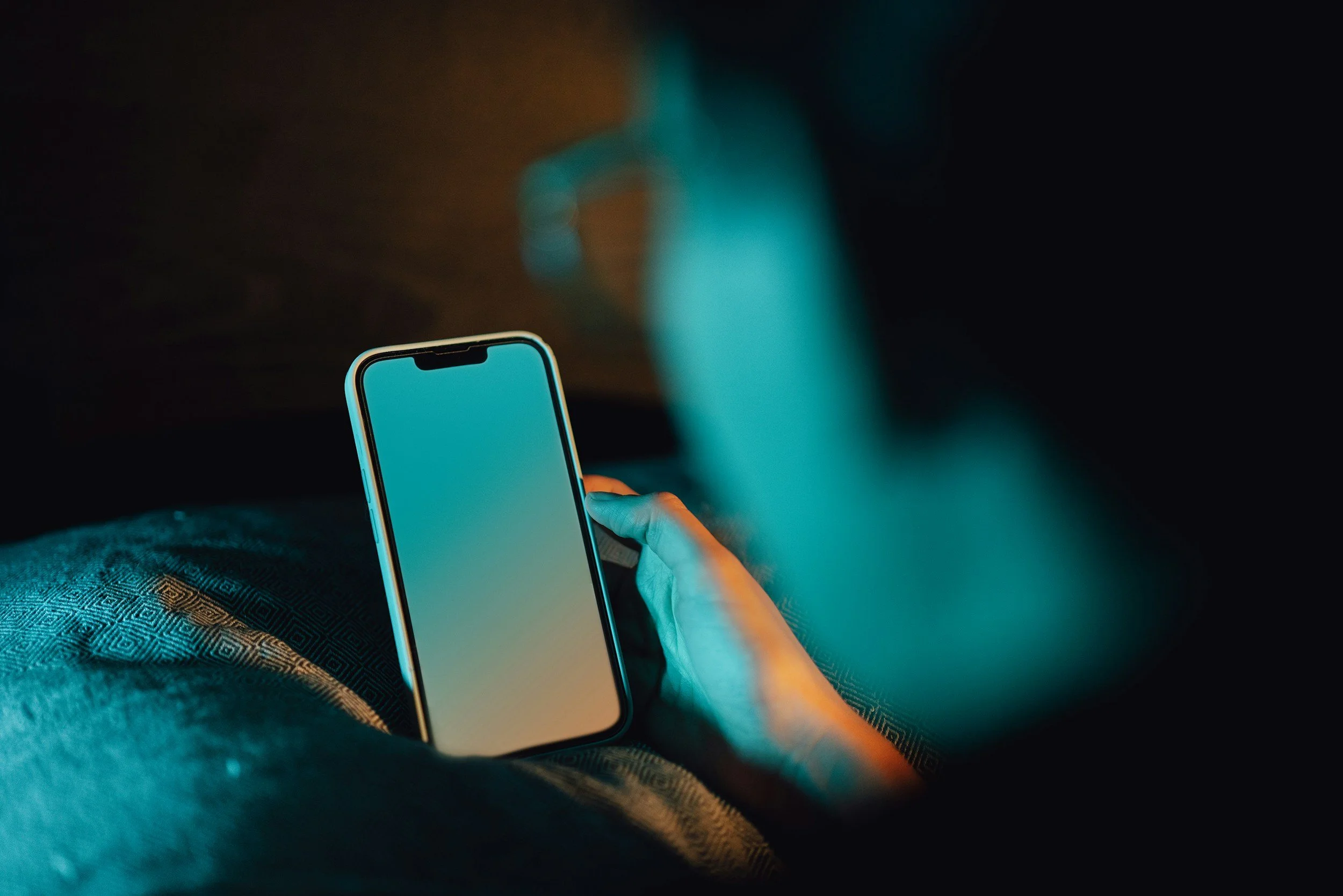 Person holding a smartphone in their hand in a dimly lit room.