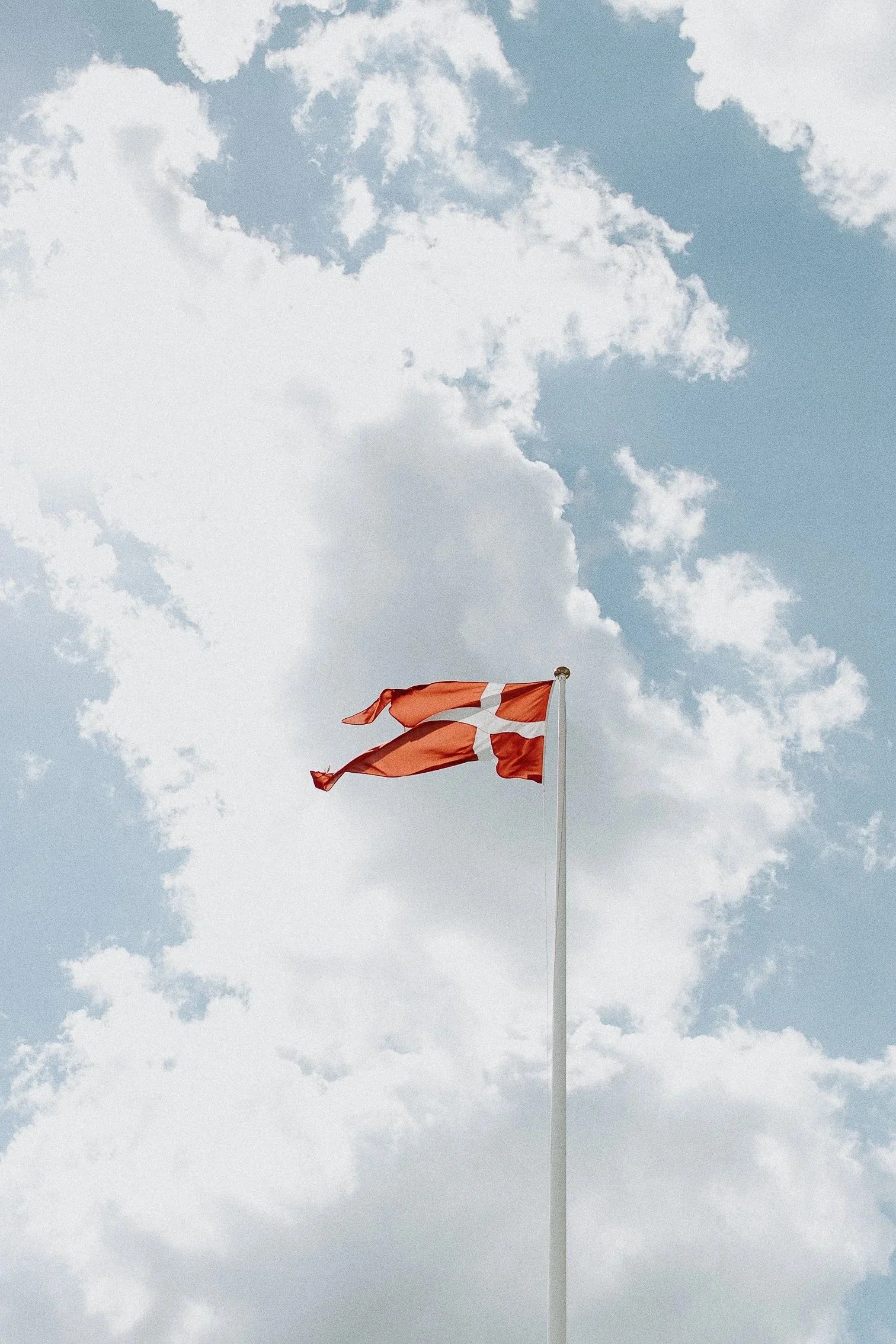 Dansk flagg som vaier i vinden mot en delvis skyet himmel.