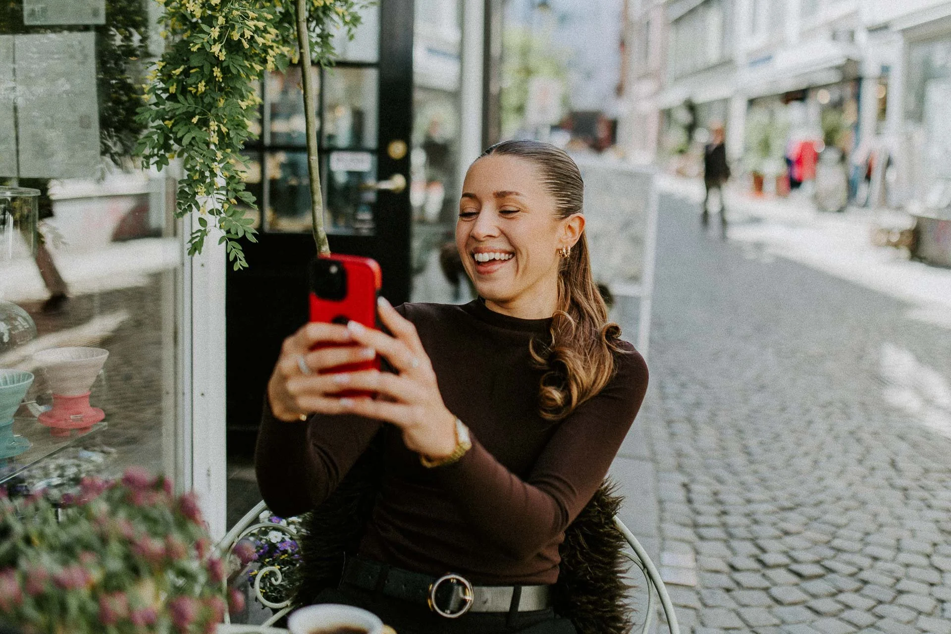 Reklamefotografering til kampanje for Altibox bedrift tatt i naturlig lys kvinne som tar bilde med en rød mobiltelefon sitter på en utekafe