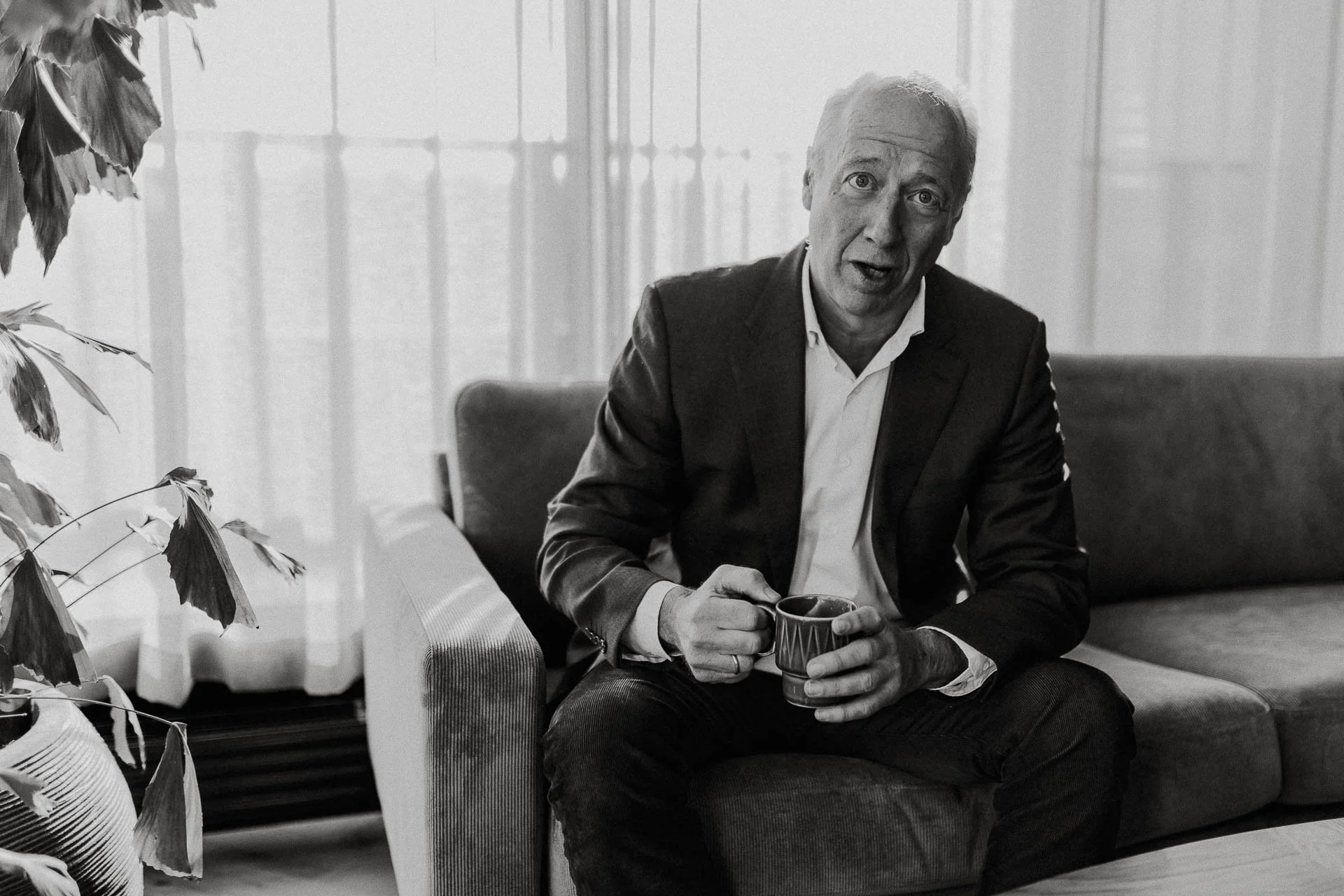 Direktør ser kamera holder kaffekopp sitter i sofaen ser alvorlig ut sort hvitt reklamefotografering for nofo norsk oljevernberedskap tatt i naturlig lys