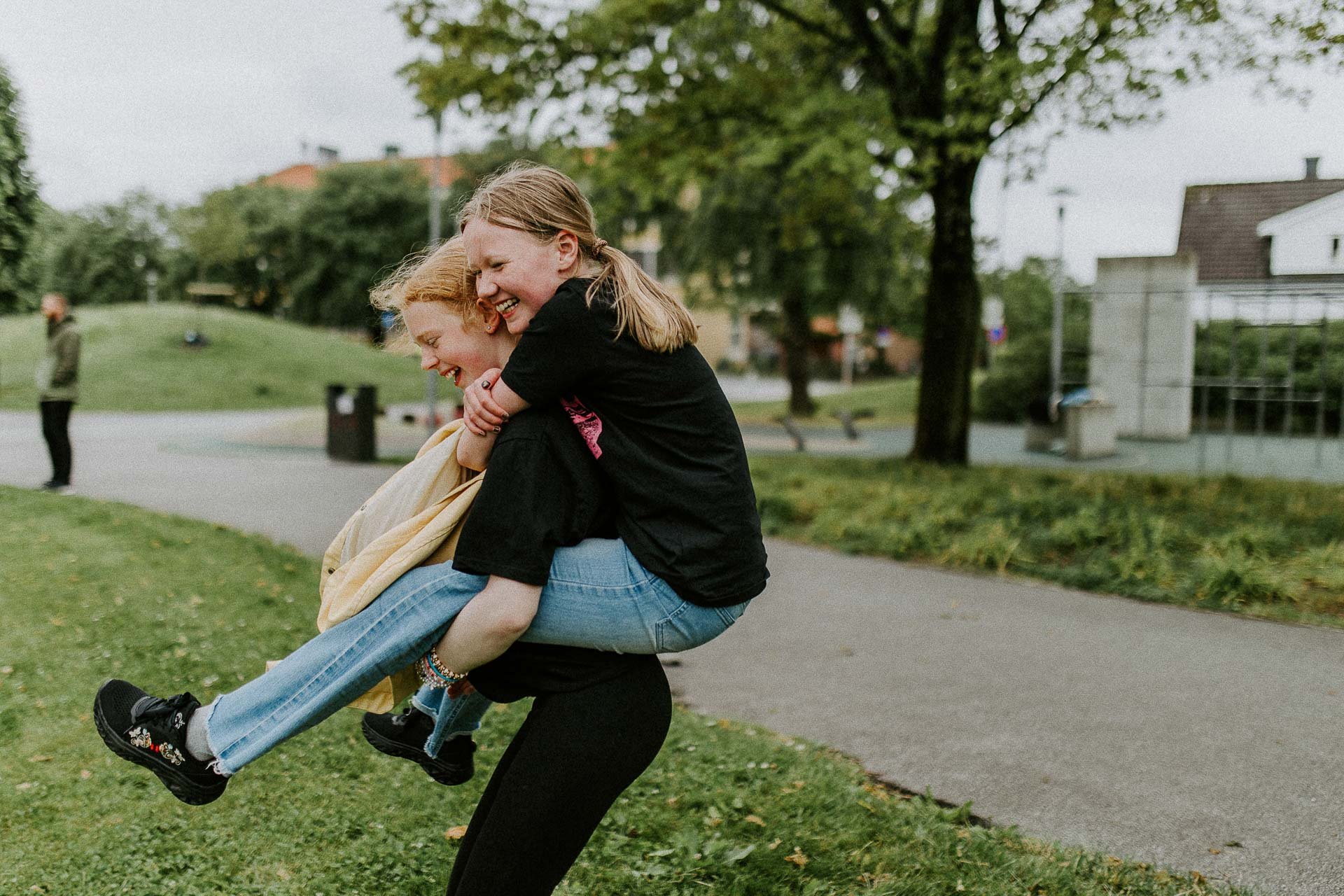To ungdommer som leker og smiler hun ene sitter på ryggen til hun andre de er i et grønt område naturlig lys, reklamefotografering for stavanger kommune, områdesatsingen i hillevåg
