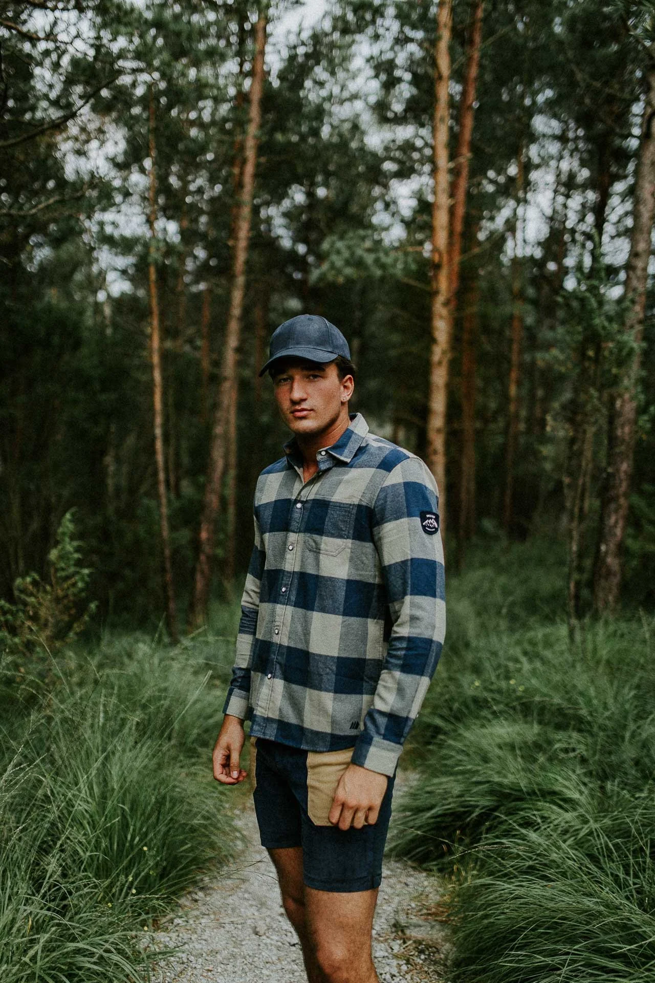 mann som står og ser i kameraet med rutete skjorte og caps med skog i bakgrunnen Reklamefotografering til kampanje for Skogstad bilder tatt i preikestolenområdet bilder av turklær