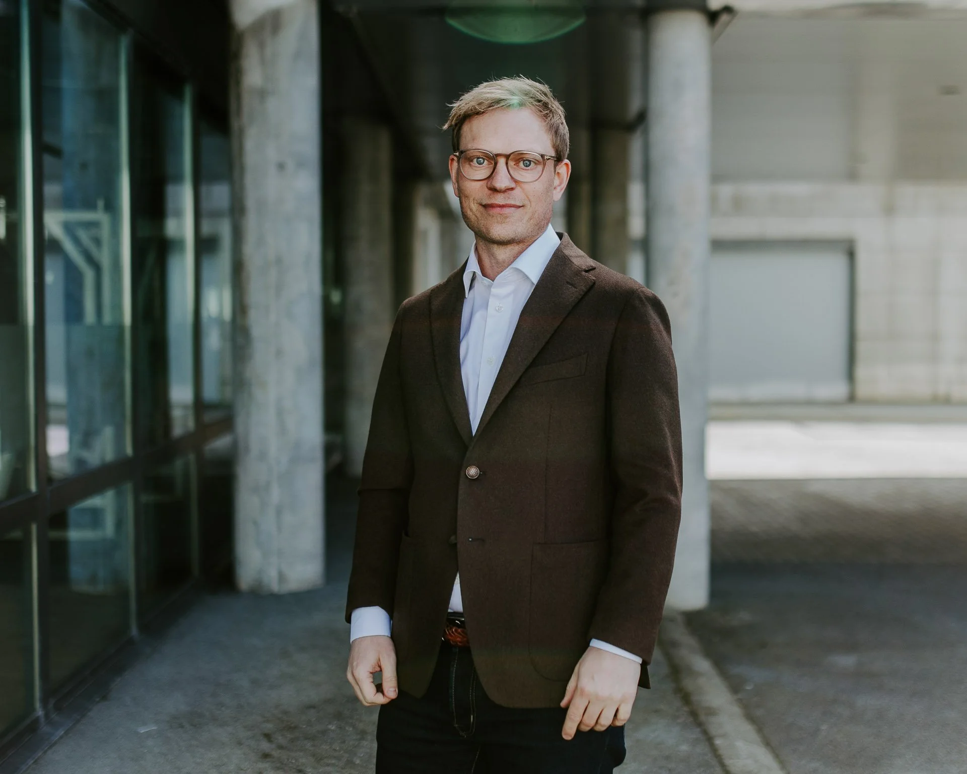 Portrett av en person som står og ser i kamera briller på halvfigur søyler i bakgrunnen rolig ansiktsuttrykk fotografering for zaptec til kampanjebruk og presse naturlig lys verksted westcontrol