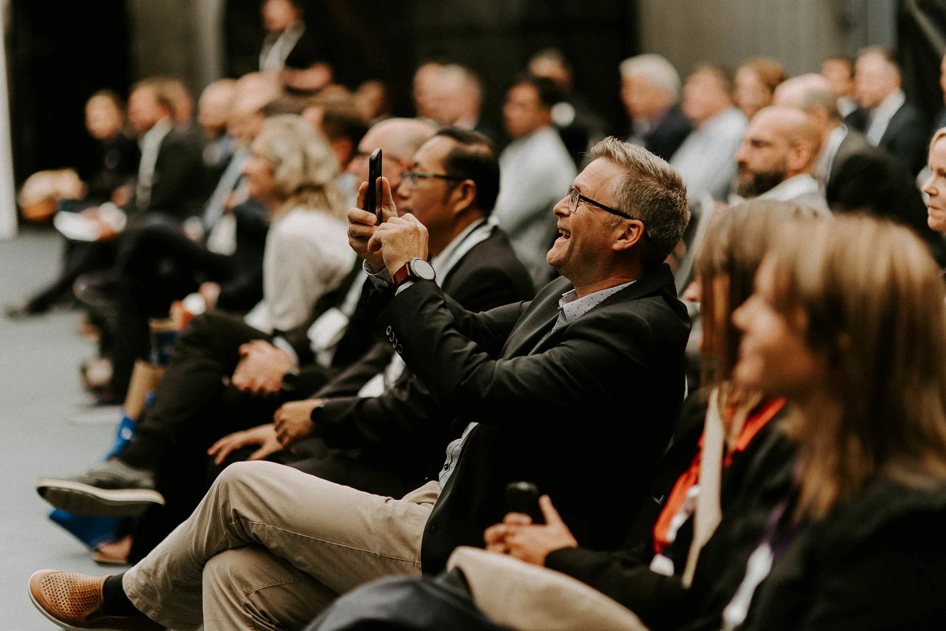 Bilde tatt under foredrag mange mennesker sitter i publikum og ser på en mann smiler og tar bilde med mobiltelefonen av den som står på scenen dokumentarfotografering for ONS, Offshore Northern Seas i Stavanger, stavanger forum