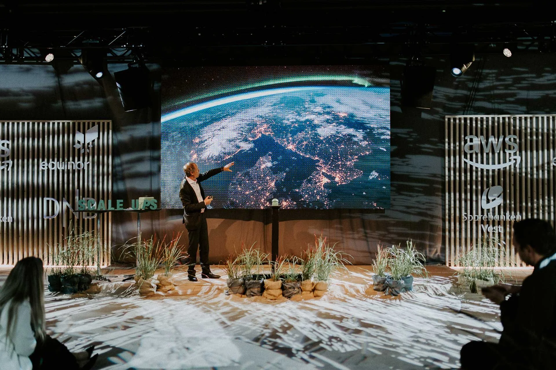 En som står på scenen og forklarer noe viser en skjerm med bilde av jordkloden som han peker på dokumentarfotografering for ONS, Offshore Northern Seas i Stavanger, stavanger forum