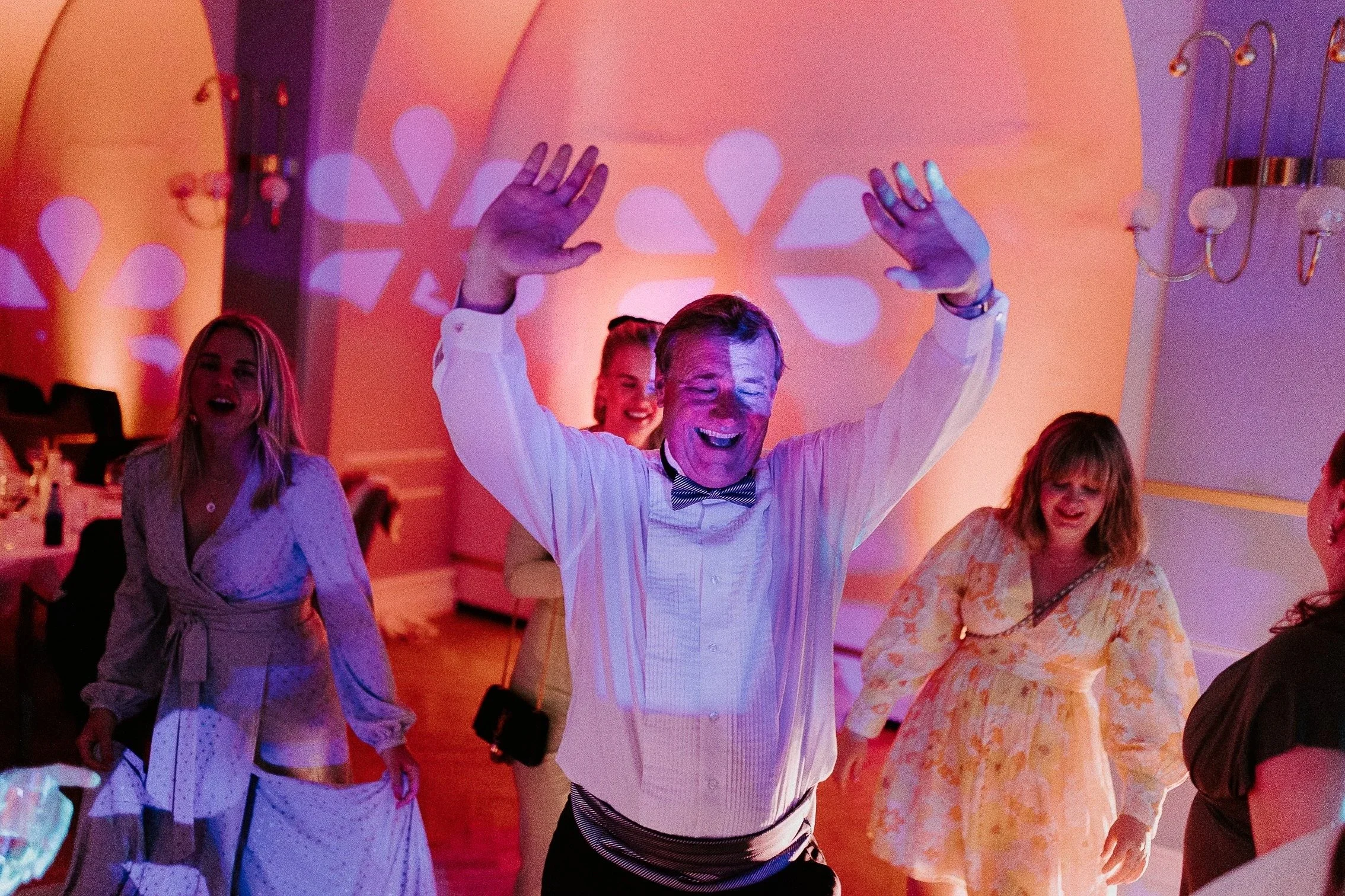 Mennesker som danser og har det gøy på fest, med farget lys og blomstrete veggdekor.