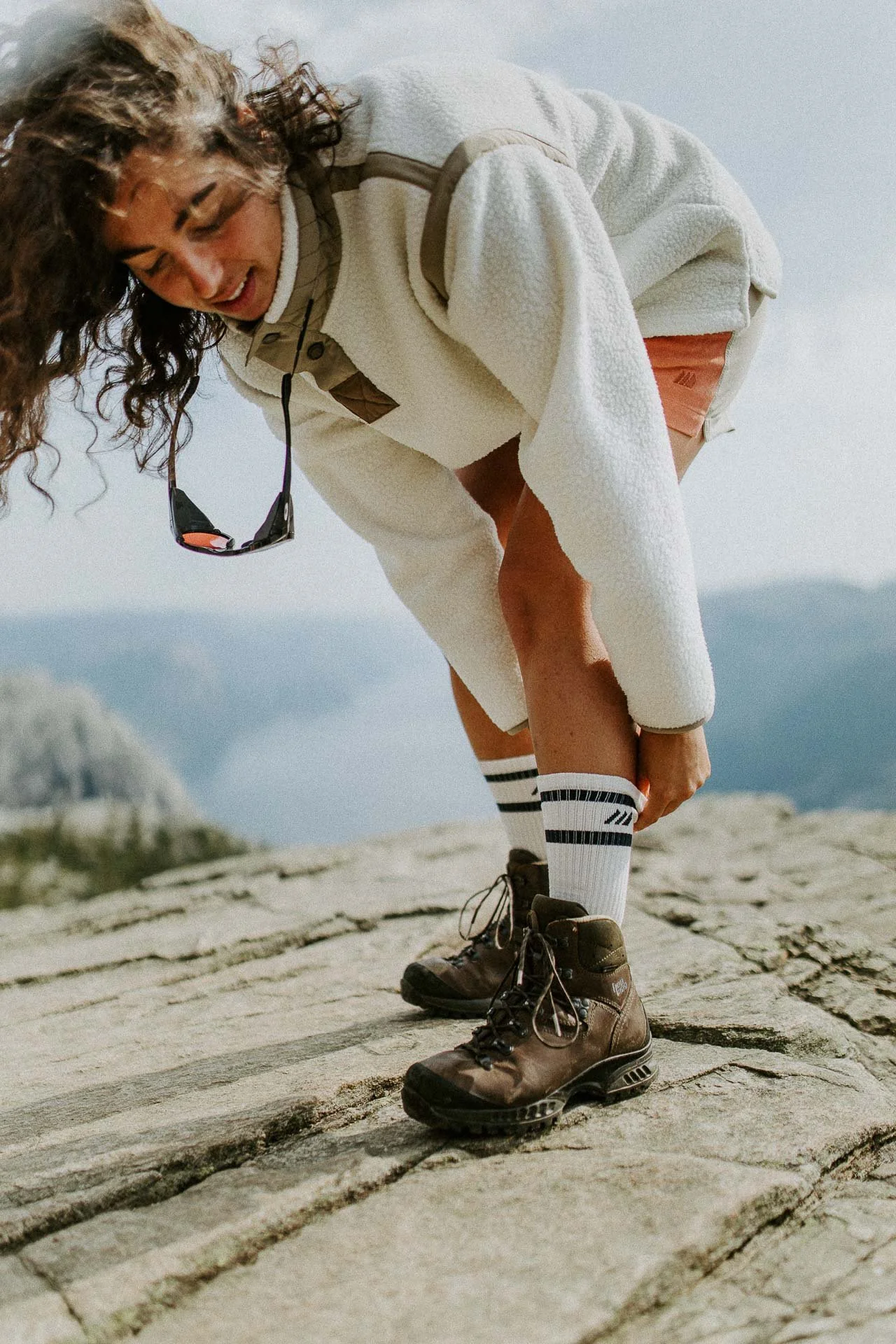 Bilde av kvinne som tar på seg sokker bildet er i bevegelse tatt på preikestolen med utsikt mot fjorden Reklamefotografering til kampanje for Skogstad bilder tatt i preikestolenområdet bilder av turklær