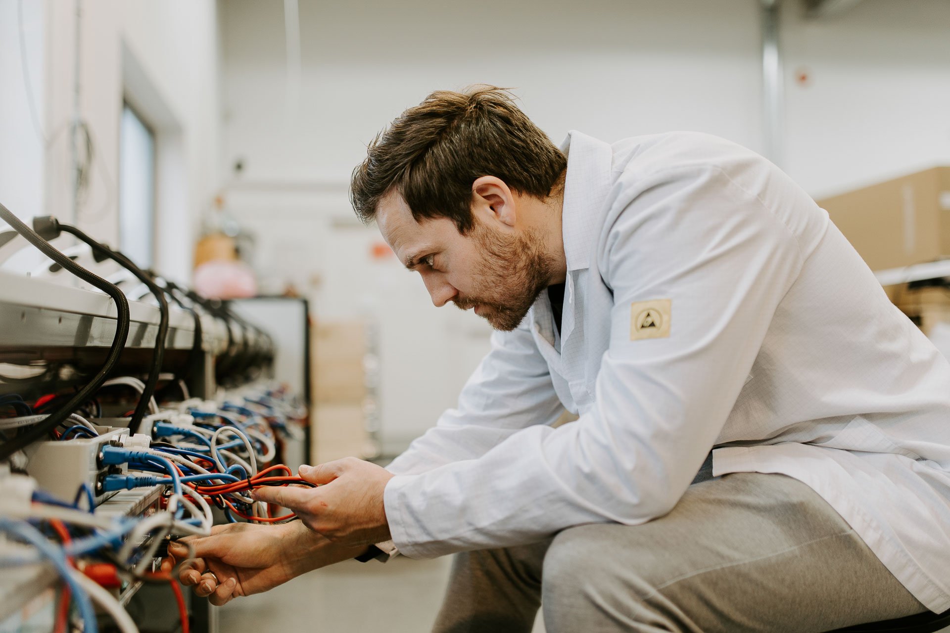 Portrett av mann i arbeid sitter og jobber med mange ledninger på venstre side har på hvit jakke fotografering for zaptec til kampanjebruk og presse naturlig lys verksted westcontrol