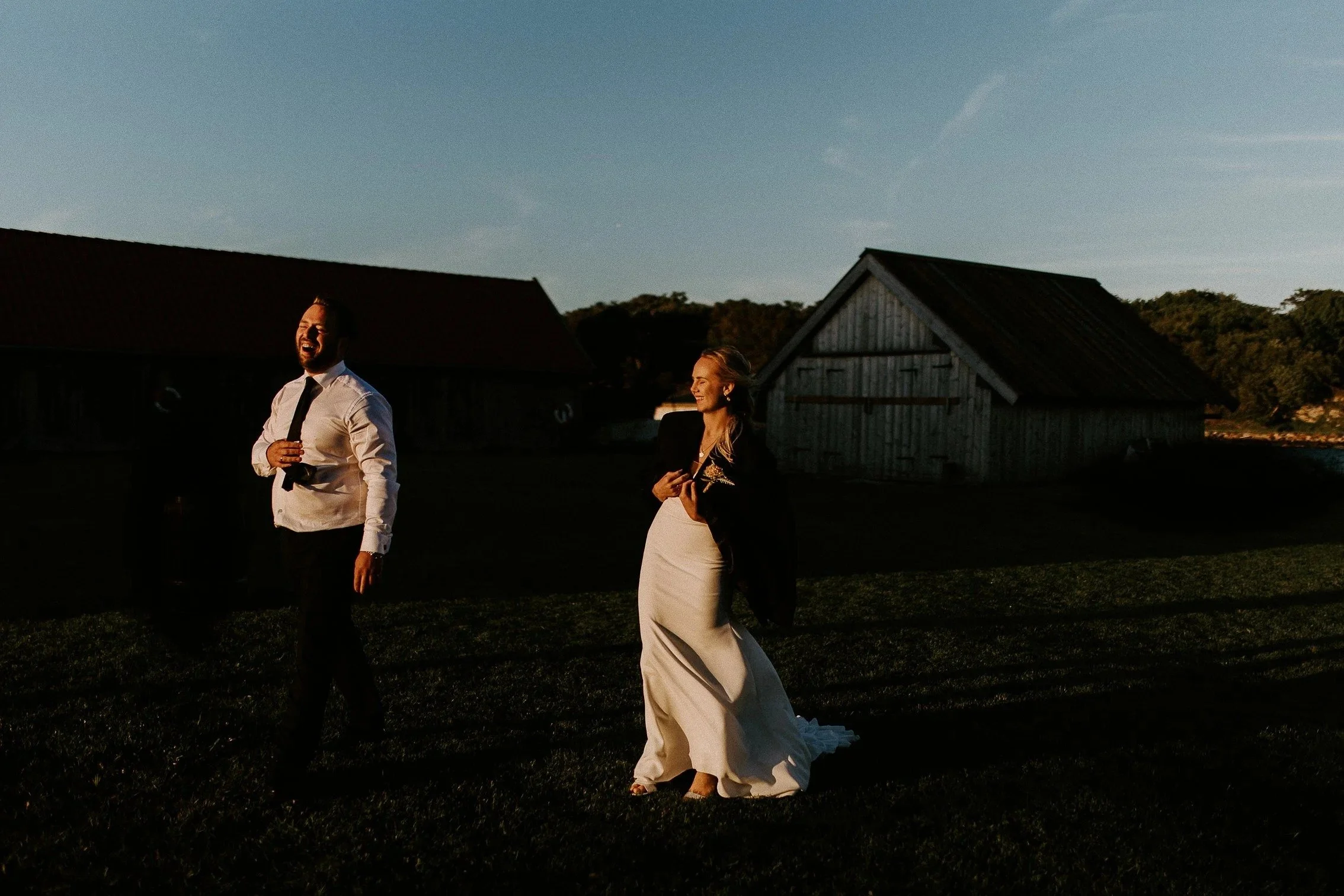 En mann og kvinne nyter et øyeblikk utendørs i solnedgang, med rustikke låver i bakgrunnen.