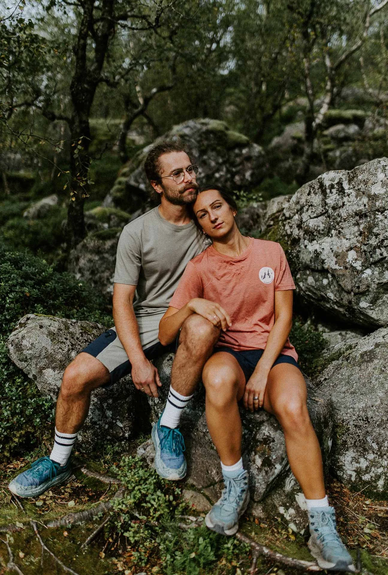 Et kjærestepar som sitter på steiner stein og skog i bakgrunn rosa og beige tsjorte shorts på Reklamefotografering av modeller til kampanje for Skogstad bilder tatt i preikestolenområdet bilder av turklær