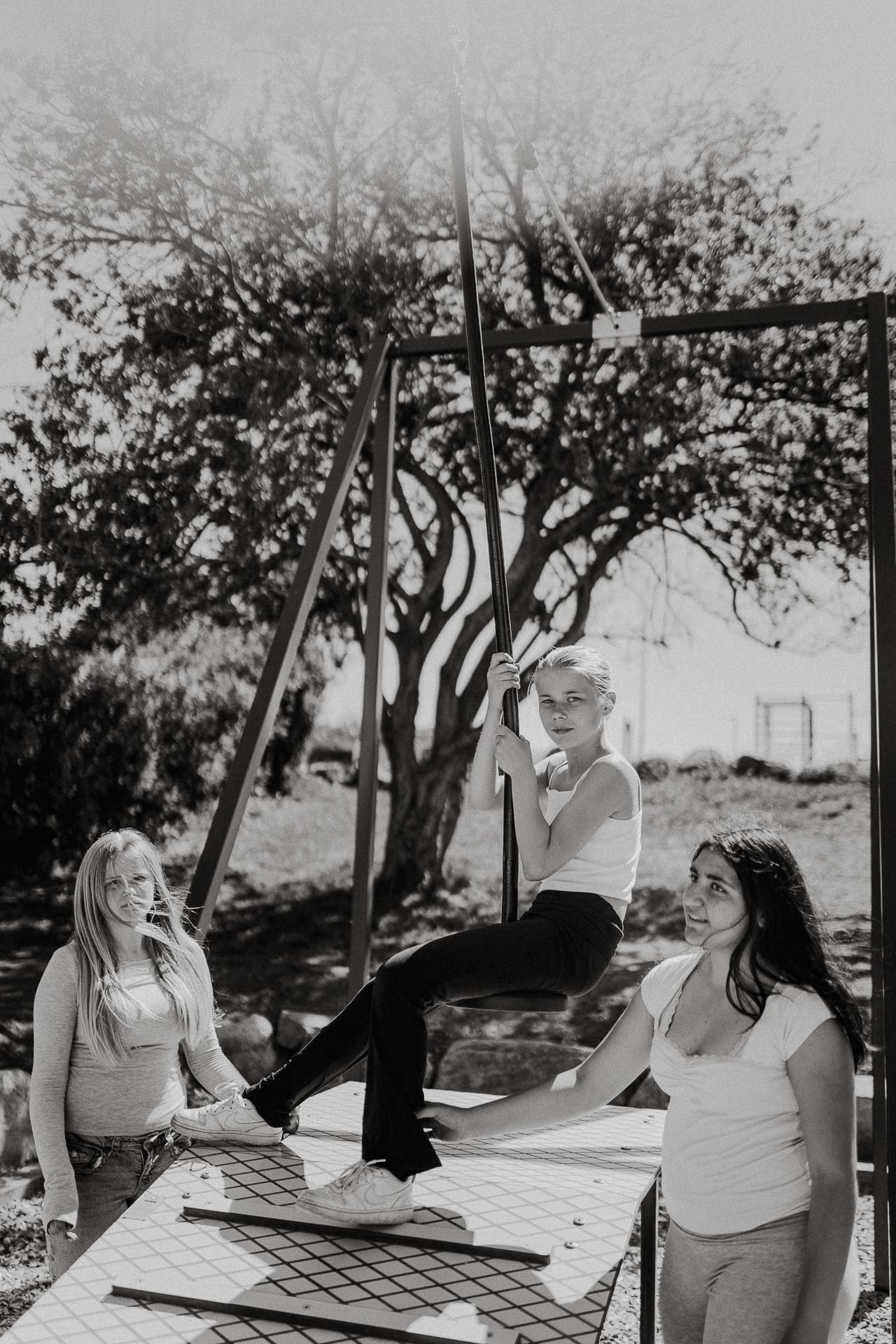 Sort hvitt portrett av tre skoleelever to av de ser mot kamera en til side hun sitter på en zipline alvorlig uttrykk vind i hår naturlig lys, reklamefotografering for stavanger kommune, områdesatsingen på kvernevik tatt på sommeren