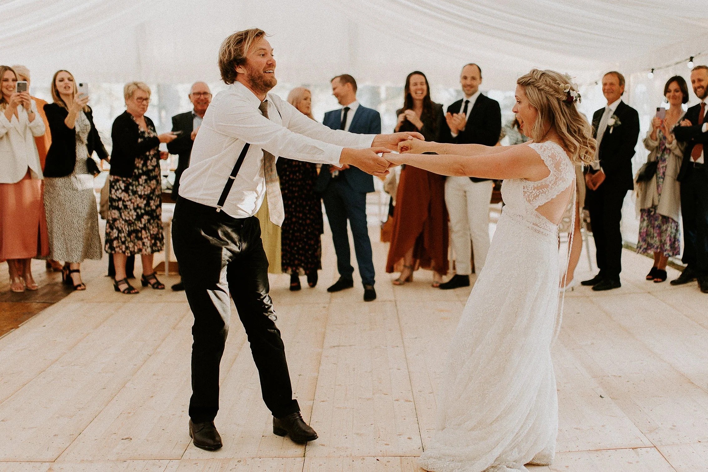 Brud og brudgom danser sammen under bryllupsfesten, med gjester som ser på og tar bilder i bakgrunnen.