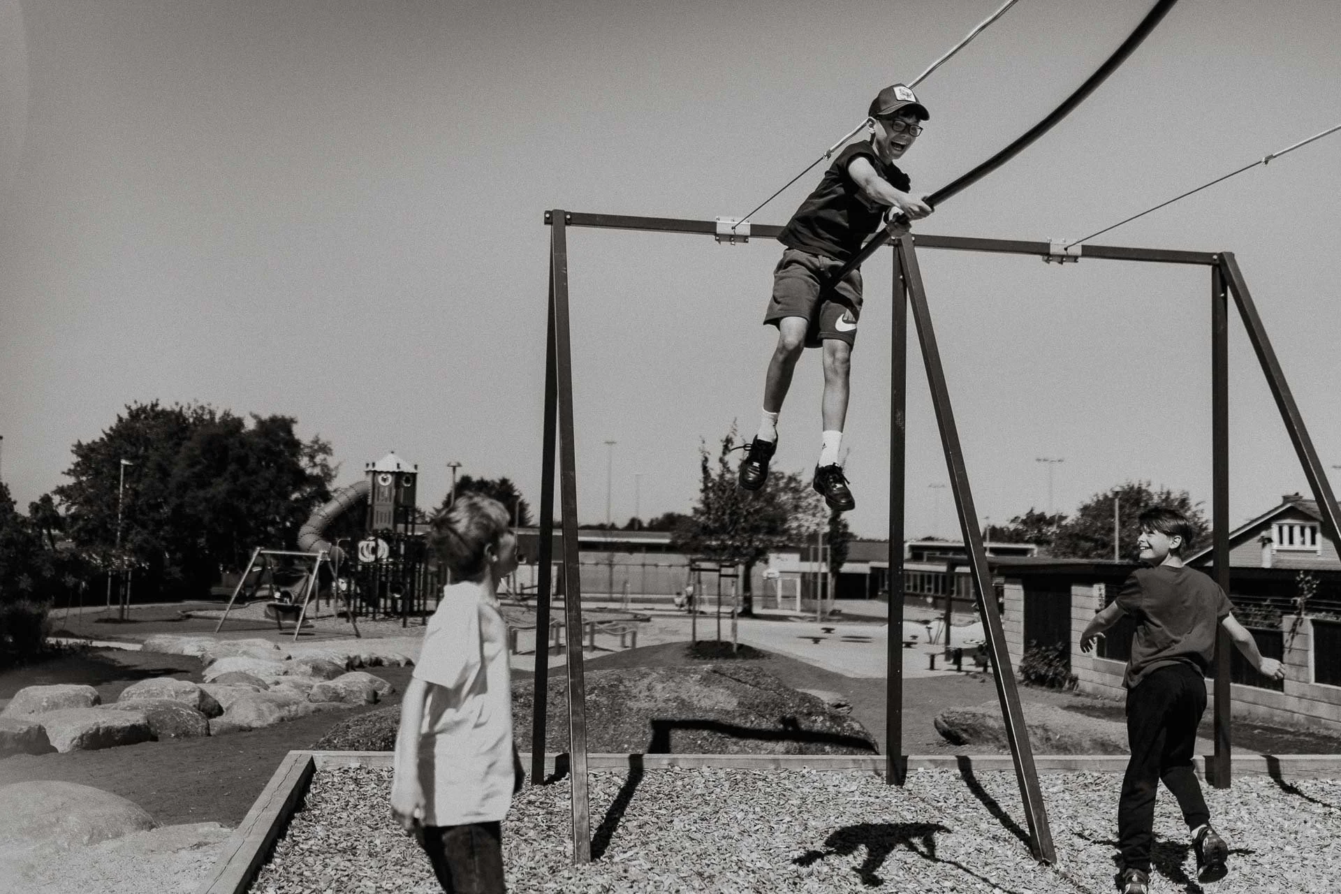 Barn som leker i skolegård tre gutter han ene er på zipline høyt oppe i luften med bevegelse naturlig lys, reklamefotografering for stavanger kommune, områdesatsingen på kvernevik tatt på sommeren