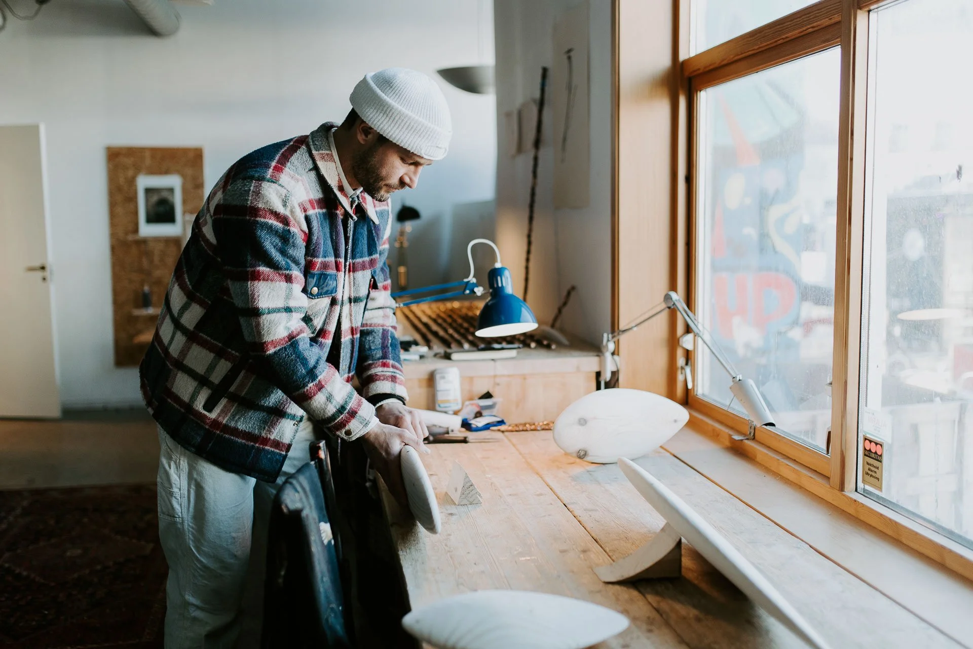 Person i arbeid inne på verksted han har rutete jakke og hvit lue på ser konsentrert ut ned mot det han jobber med naturlig lys, reklamefotografering for stavanger kommune, områdesatsingen på Storhaug tatt på vinteren i snø og lav sol