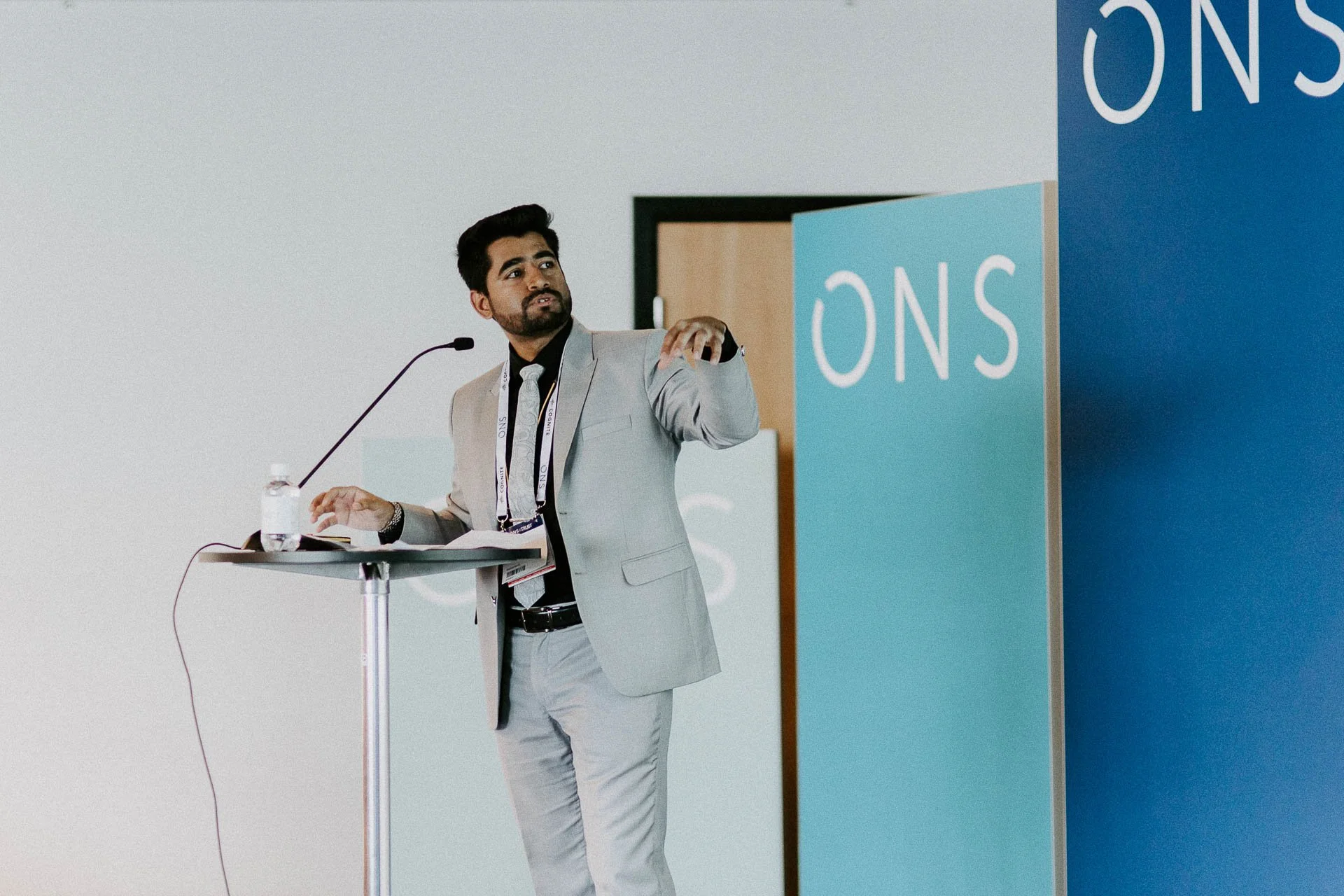 Foredragsholder står ved bord med mikrofon og forteller noe og peker ons logoer er tydelig synlige på blå rollup dokumentarfotografering for ONS, Offshore Northern Seas i Stavanger, stavanger forum