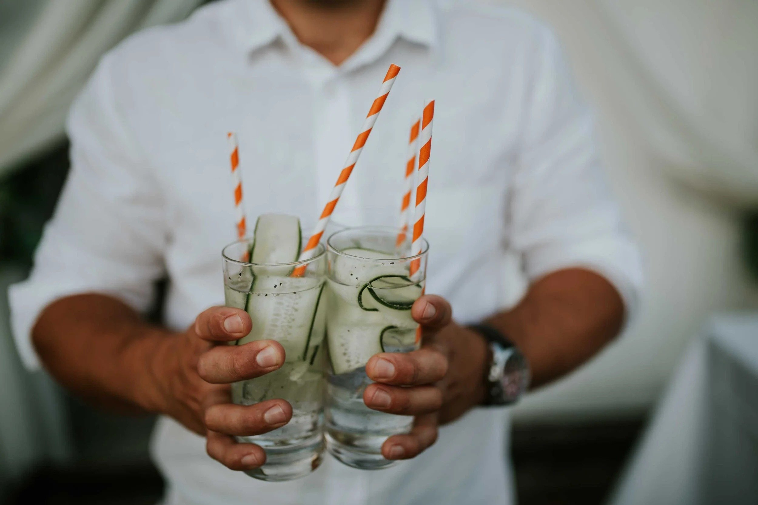 En person holder to glass med agrurk drinker med stripete sugerør.