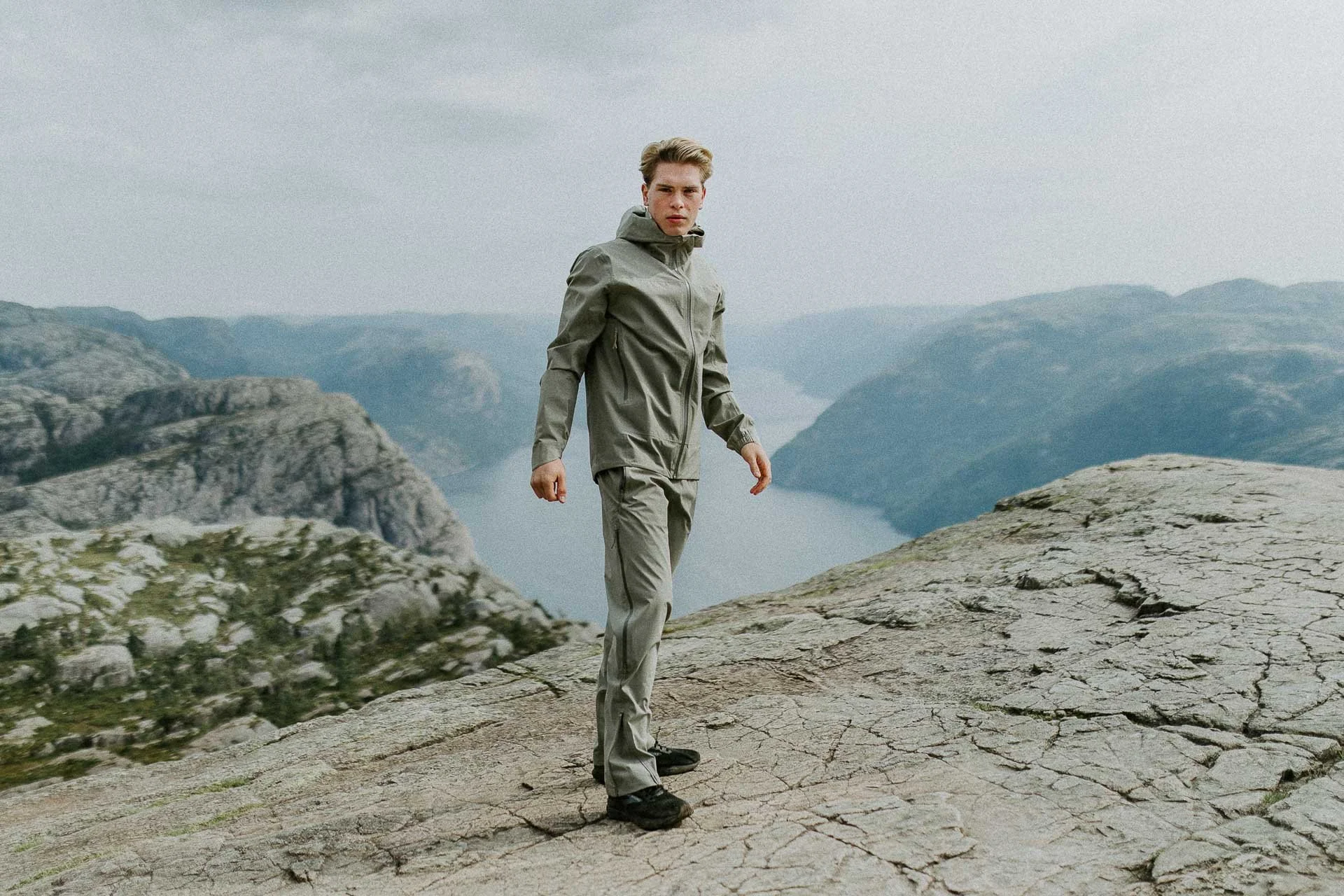 mann som står på preikestolen ser i kameraet i helfigur fjord i bakgrunen Reklamefotografering av modeller til kampanje for Skogstad bilder tatt i preikestolenområdet bilder av turklær