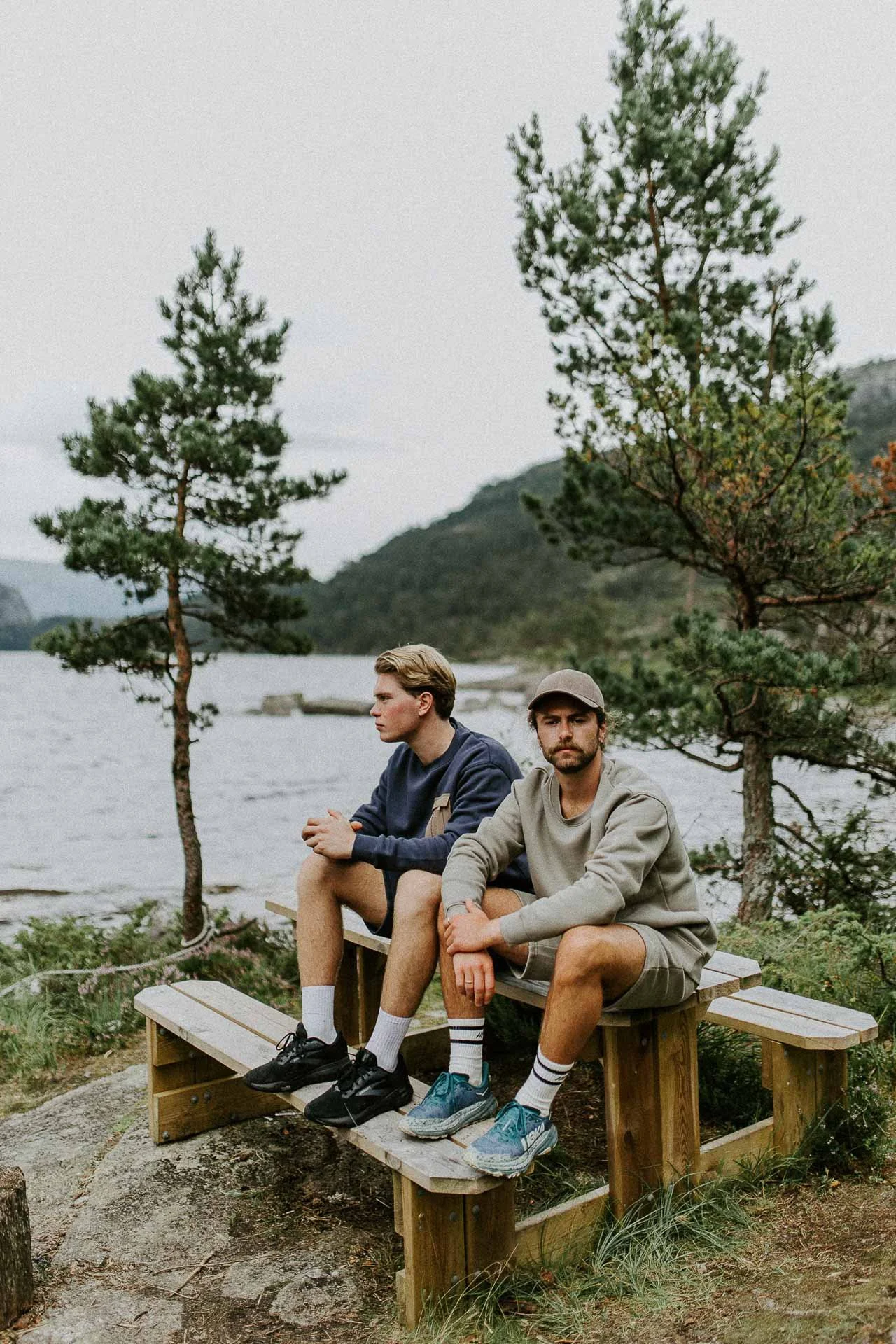 To menn sitter på benk Caps på en ser i kamera en ser til siden skog fjell og sjø i bakgrunnen Reklamefotografering av modeller til kampanje for Skogstad bilder tatt i preikestolenområdet bilder av turklær