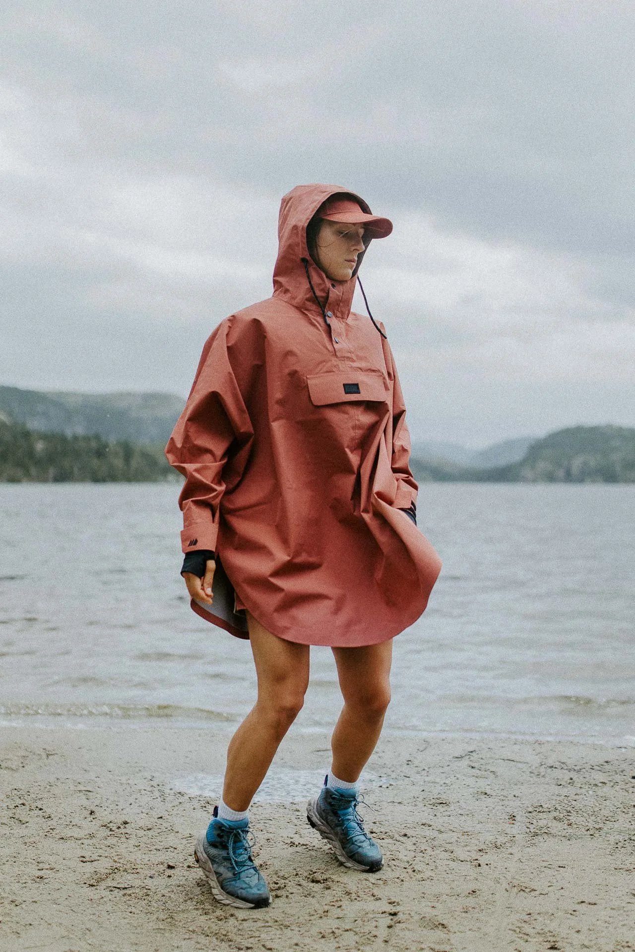 Kvinne som hopper og beveger seg på stranden vann og fjell i bakgrunnen hun har på seg en poncho og Caps rosa Reklamefotografering av modeller til kampanje for Skogstad bilder tatt i preikestolenområdet bilder av turklær