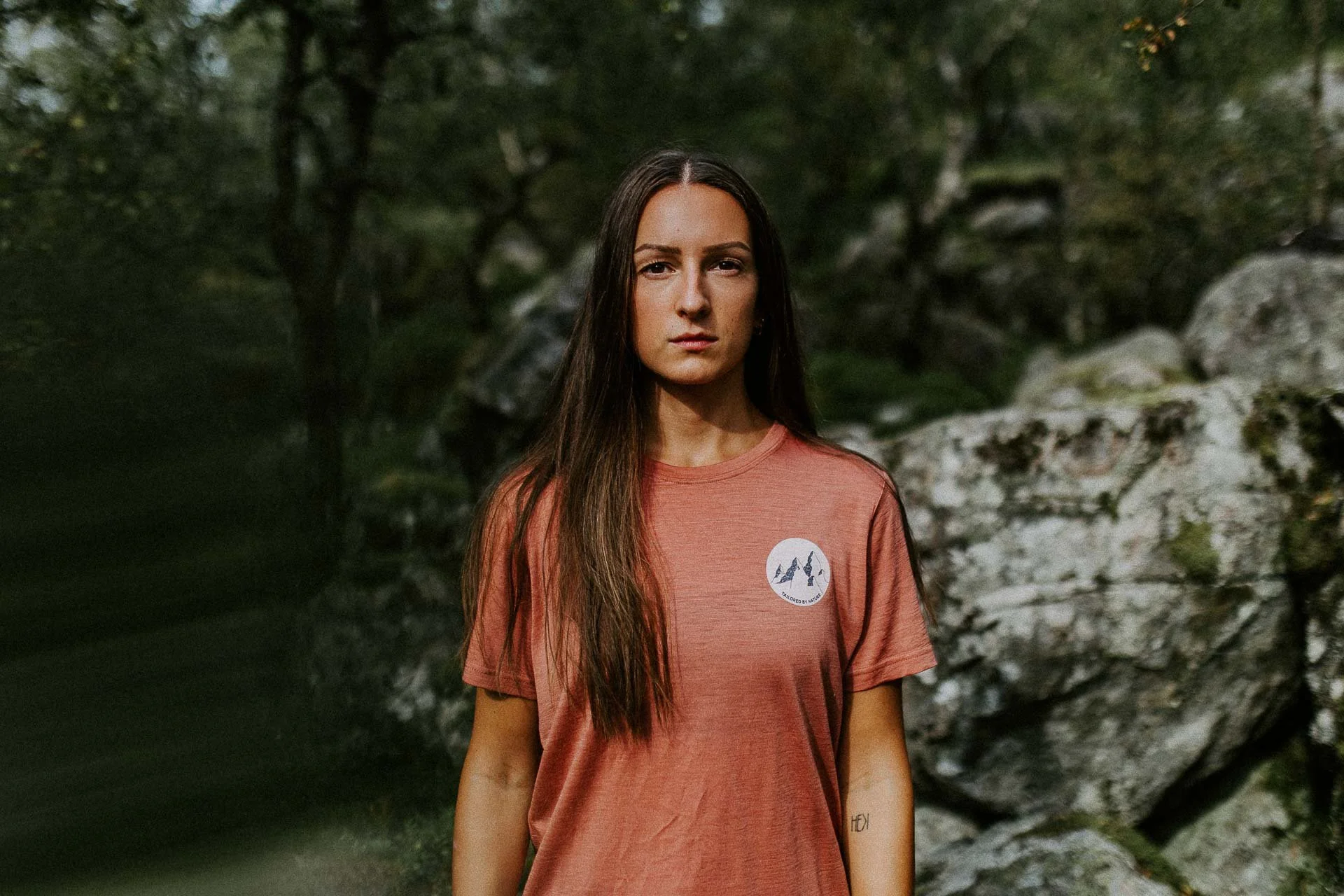 portrett av kvinne som ser rett i kameraet rosa t-skjorte med logo på fjell og skog i bakgrunnen Reklamefotografering av modeller til kampanje for Skogstad bilder tatt i preikestolenområdet bilder av turklær