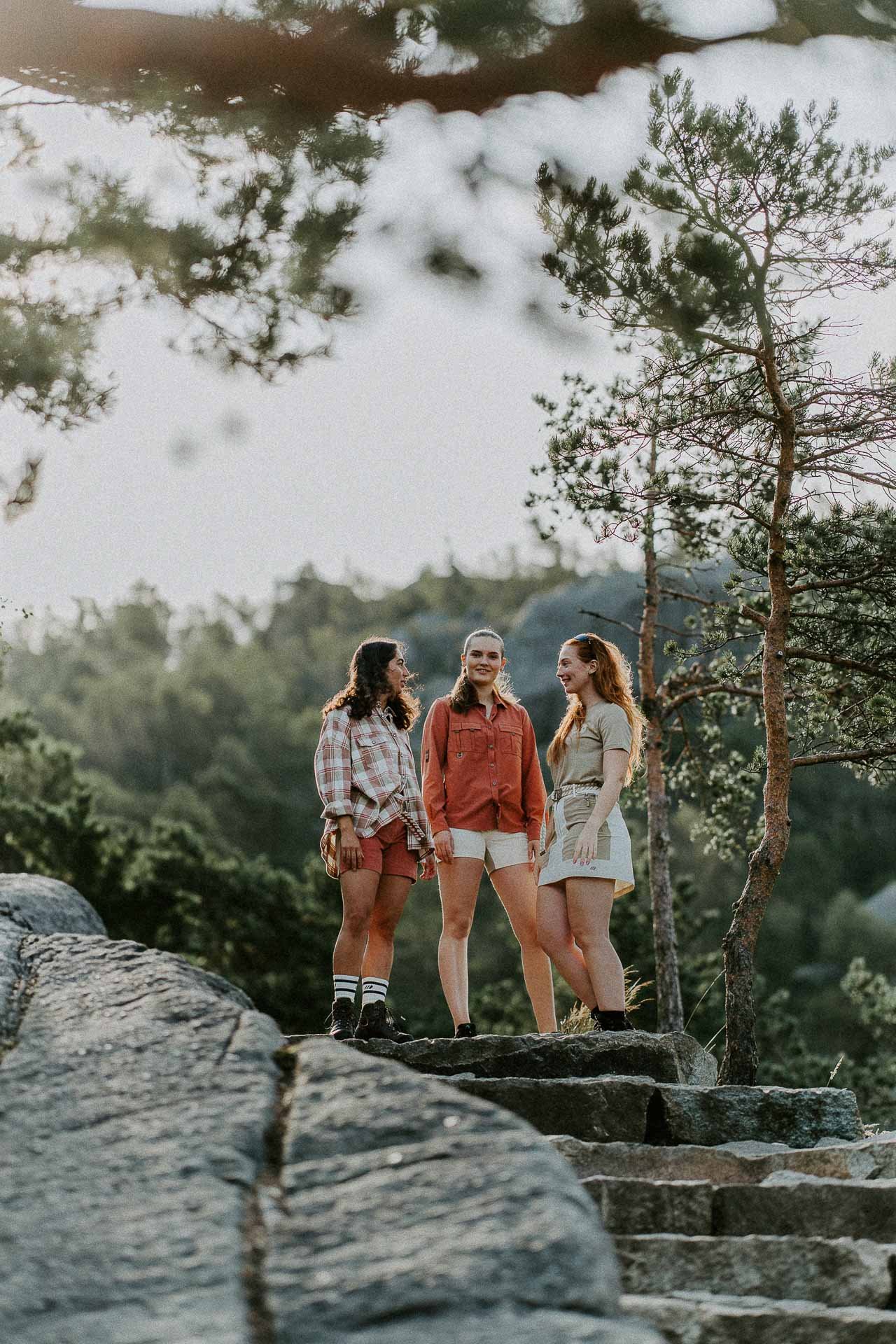 Tre kvinner står på toppen av en steintrapp fjell i bakgrunn lav sollys har på tur skjorte og shorts Reklamefotografering av modeller til kampanje for Skogstad bilder tatt i preikestolenområdet bilder av turklær