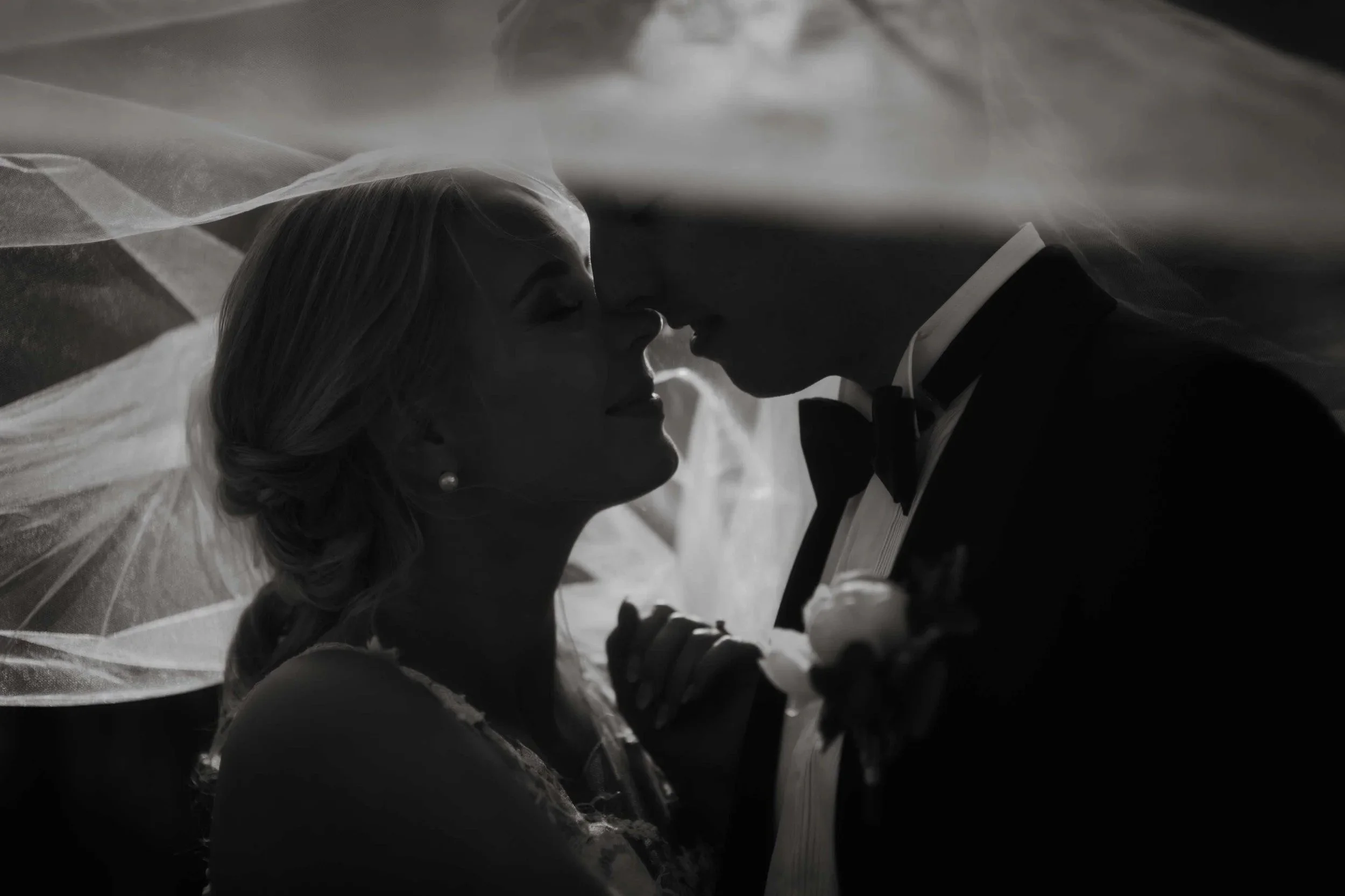 Sort hvitt bilde av brud og brudgom med ansiktene tett sammen under slør, øynene lukket.