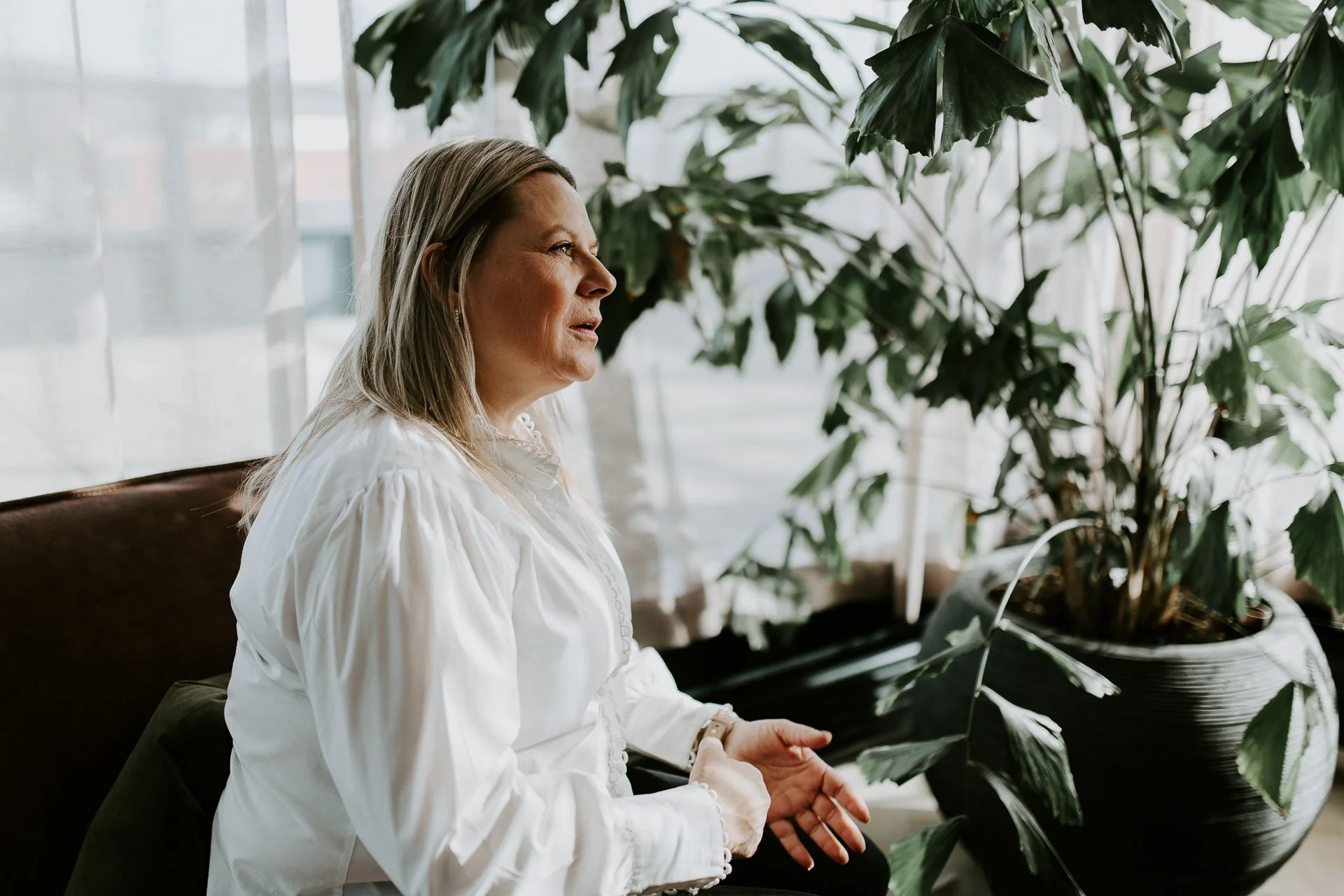 Kvinner sitter i sofa grønn plante i bakgrunnen hun ser mot person møtes situasjon reklamefotografering for nofo norsk oljevernberedskap tatt i naturlig lys