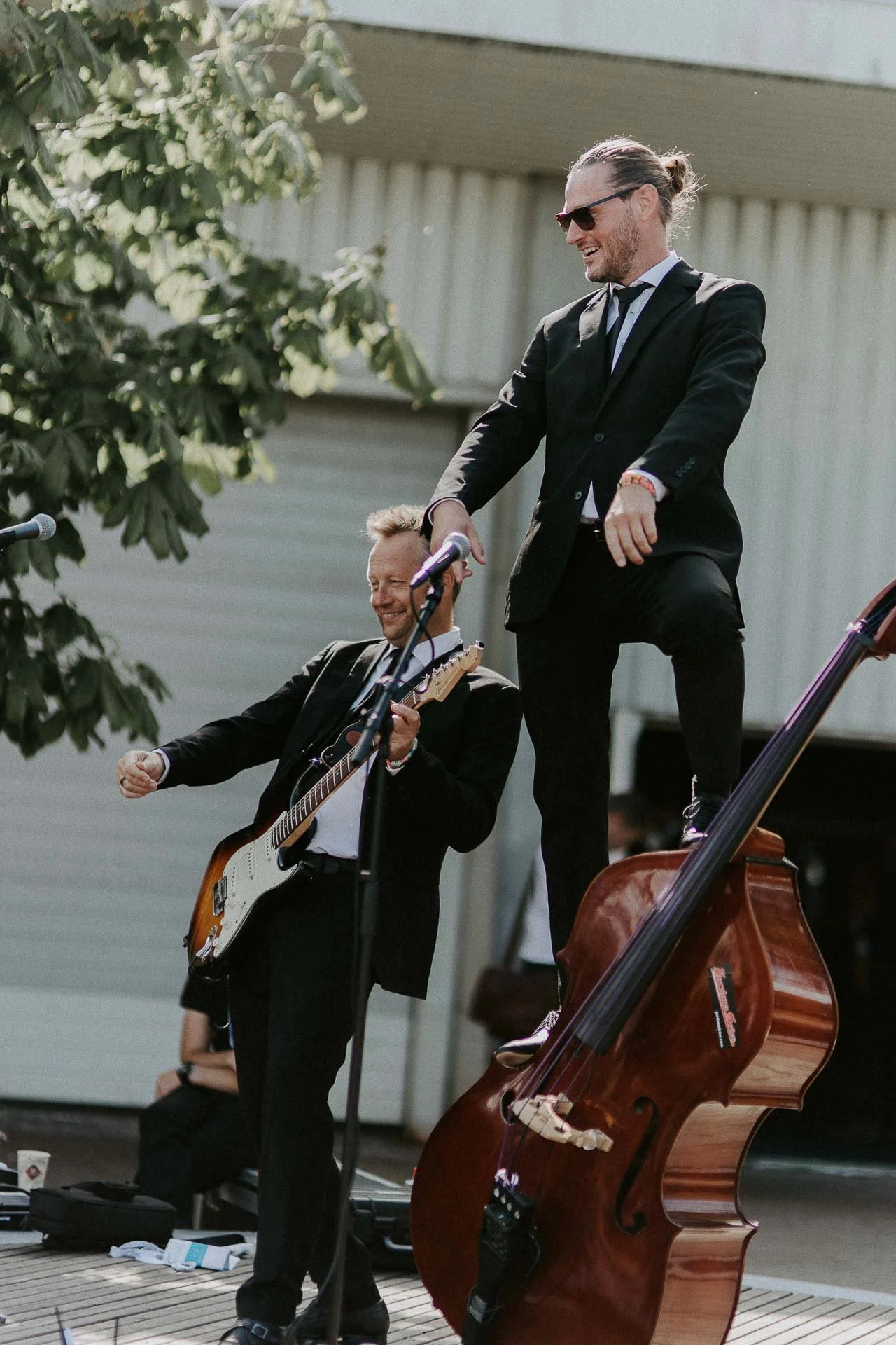 To personer spiller Iben han ene står oppå en kontrabassb tatt utendørs trær og bygge Bakgrunn dokumentarfotografering for ONS, Offshore Northern Seas i Stavanger, stavanger forum