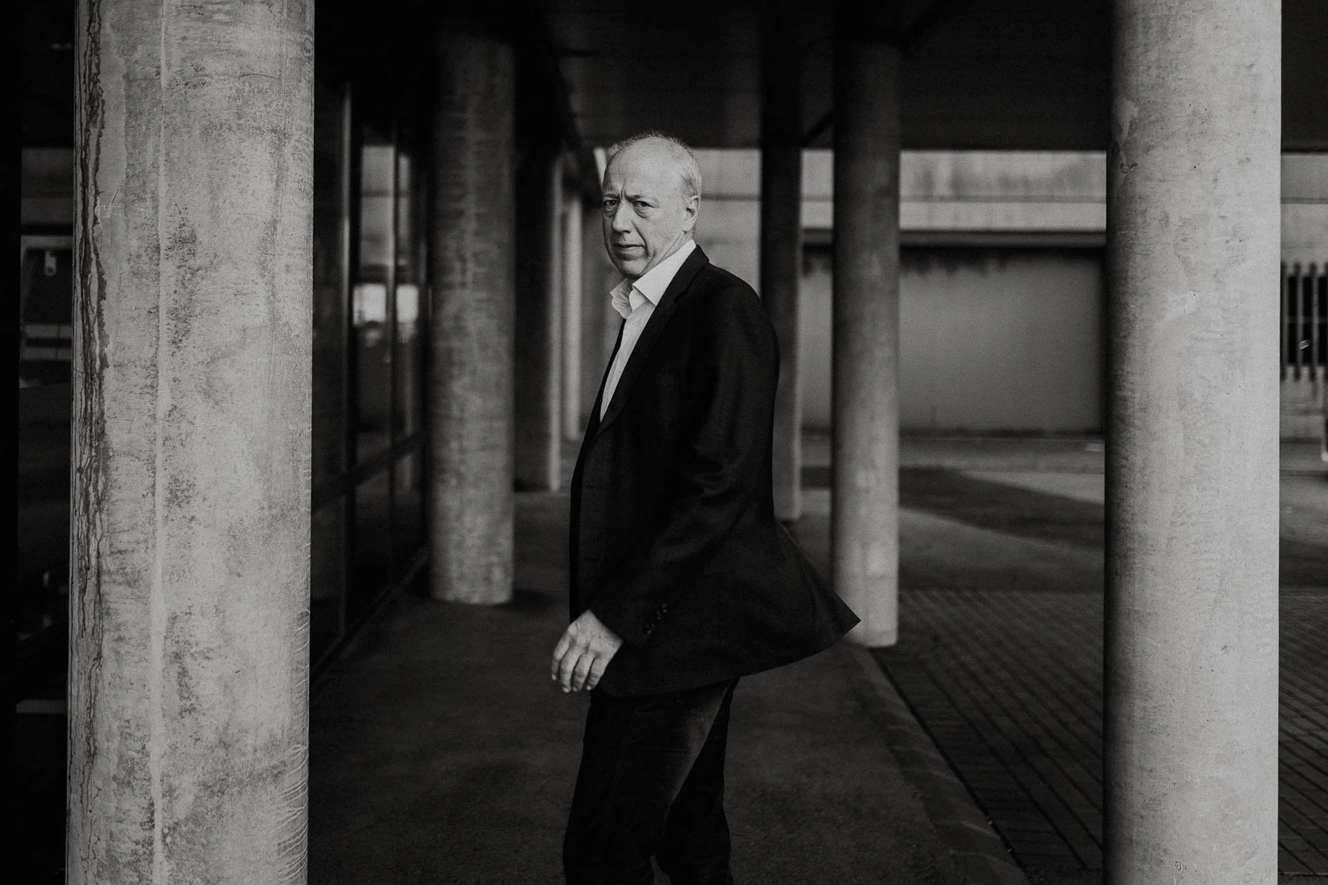 Portrett av direktør i Nofo norsk Oljevernberedskap sorthvitt ser i kamera alvorlig helfigurbilde han står mellom noen søyler reklamefotografering for nofo norsk oljevernberedskap tatt i naturlig lys