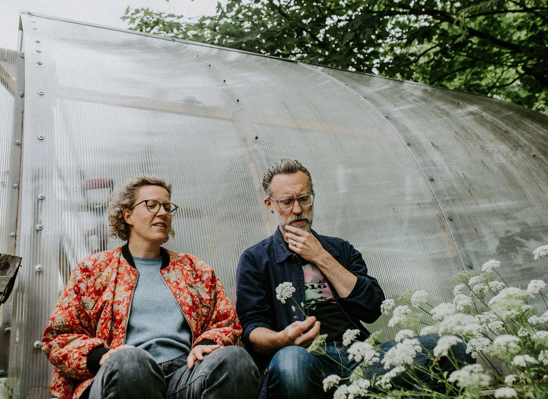 En kvinne og en mann i dypt diskusjon utenfor et drivhus mange hundekjeks i forgrunn og grønt tre i toppen naturlig lys, reklamefotografering for stavanger kommune, områdesatsingen i hillevåg