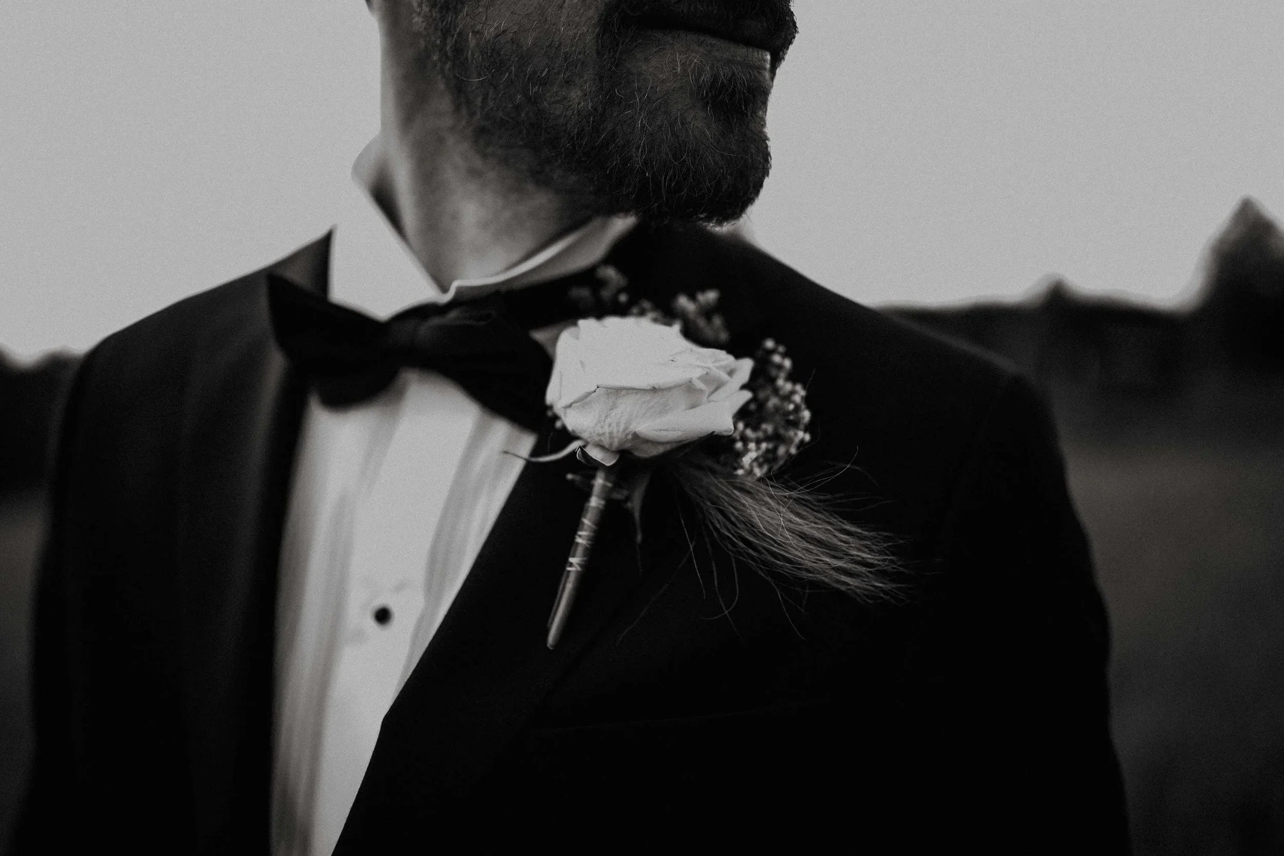 Nærbilde av en mann i formell smoking med sløyfe, hvit skjorte og brystblomst med hvit rose. Sort hvitt bilde, deler av ansiktet er synlig.