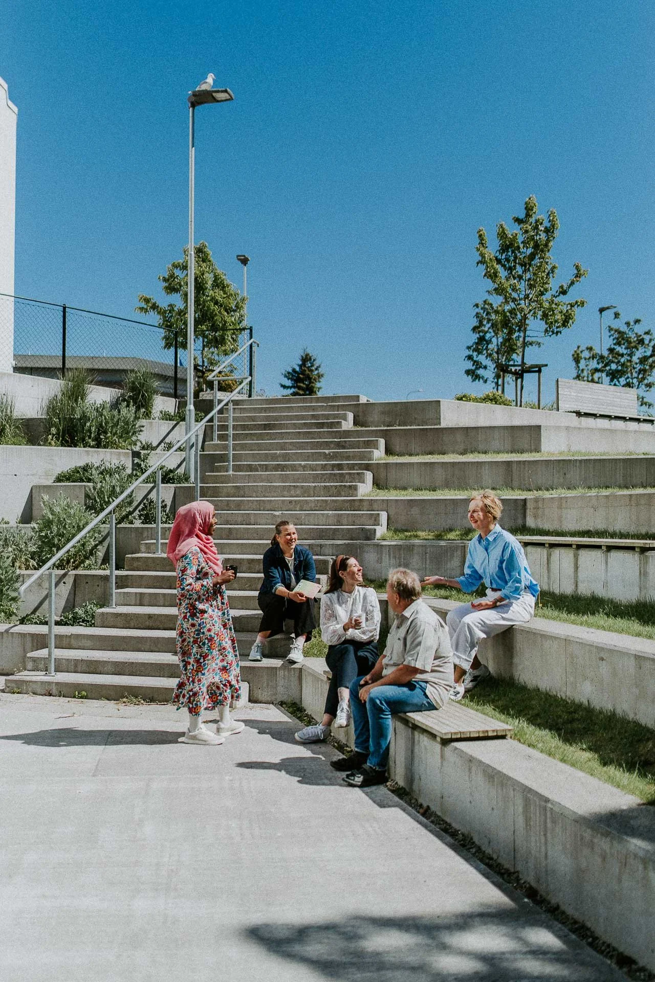 Flere personer i pausesituasjonen utendørs samtale smiler trapp i bakgrunnen og sitter i trapp en står naturlig lys, reklamefotografering for stavanger kommune, områdesatsingen på kvernevik tatt på sommeren