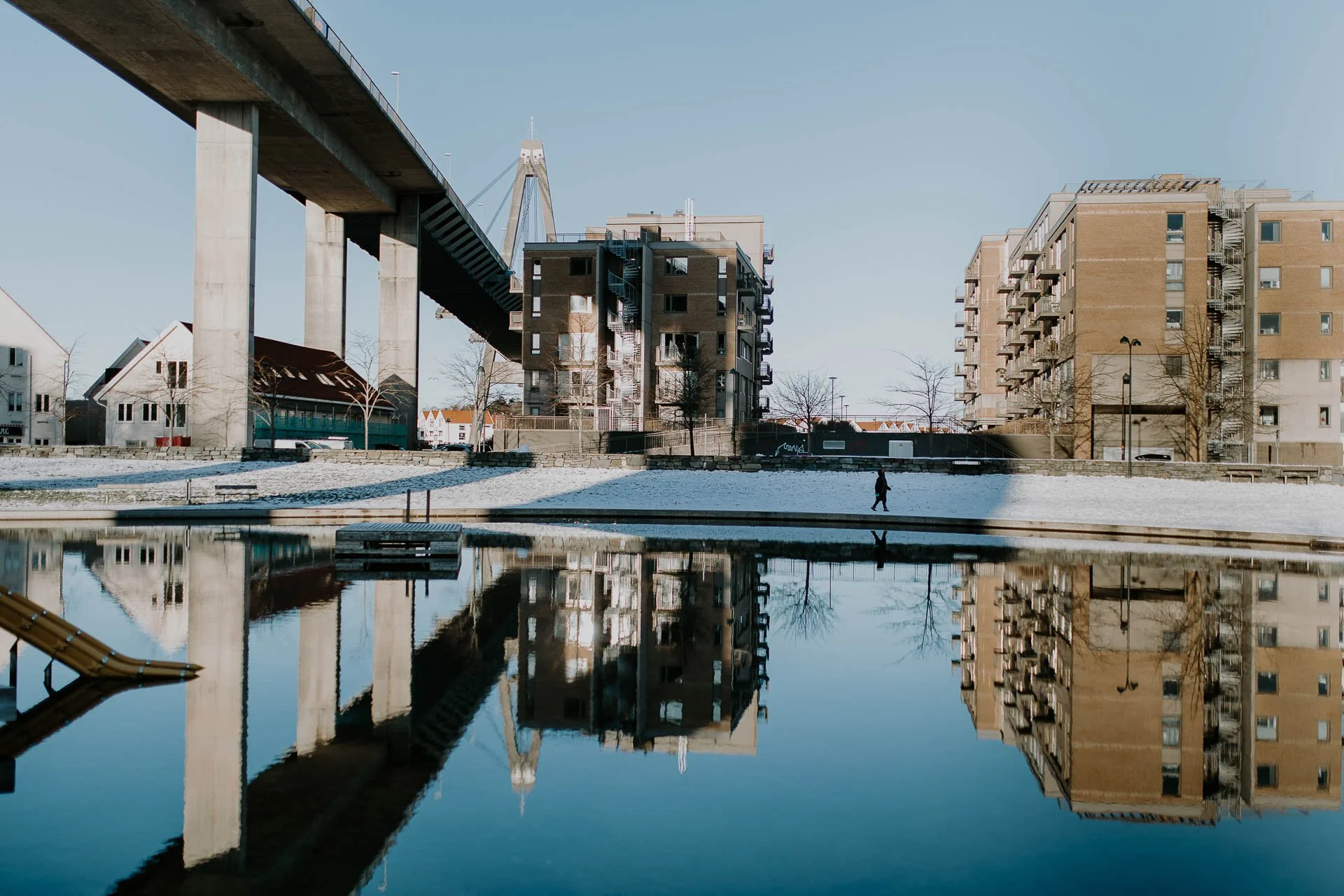 Bybrua badedammen og blokker et menneske som går langs vannet refleksjon i vannet naturlig lys, reklamefotografering for stavanger kommune, områdesatsingen på Storhaug tatt på vinteren i snø og lav sol