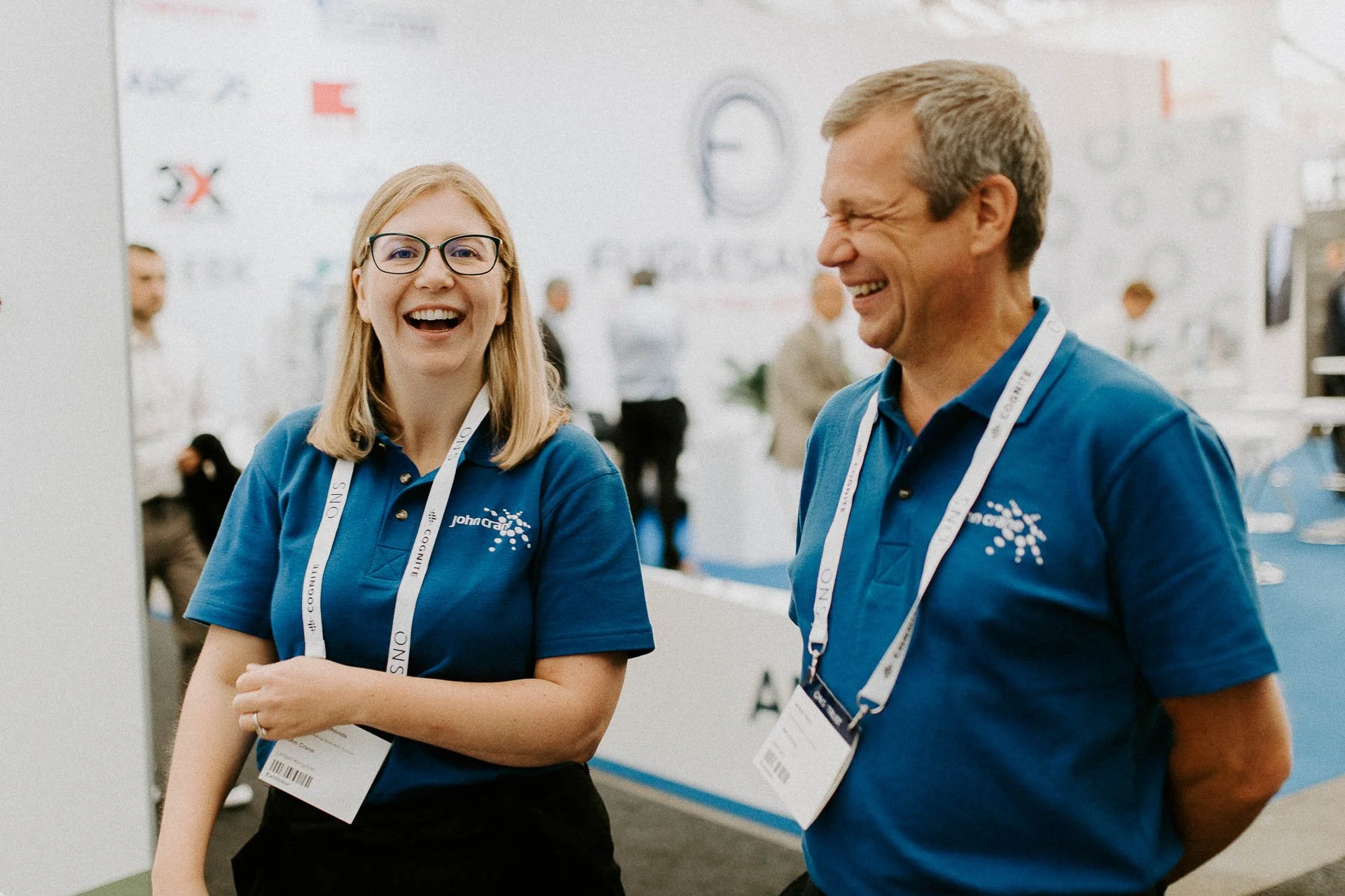 To personer som ler en kvinnes ser i kamera en man ser til siden blå skjorter adgangskort på hun har briller tatt innendørs på en stand dokumentarfotografering for ONS, Offshore Northern Seas i Stavanger, stavanger forum