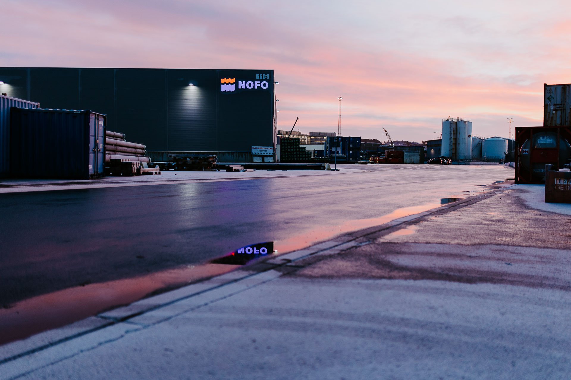 Oversiktsbilde utenfor hos norsk Oljevernberedskap morgenlys rosa og lilla farger refleksjon av logoen i vann reklamefotografering for nofo norsk oljevernberedskap tatt i naturlig lys