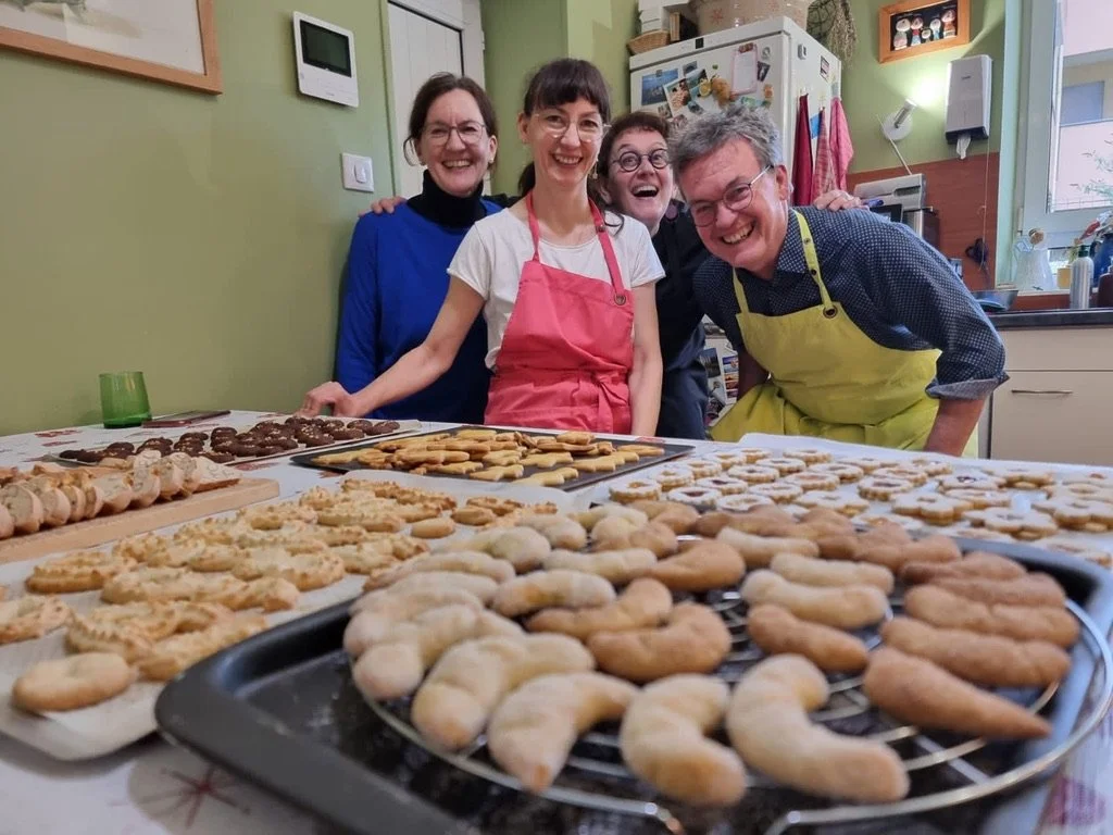 un groupe de personne souriante en arrière plan habillé de tablier et au premier plan des bredele, biscuit sablé fin alsacien