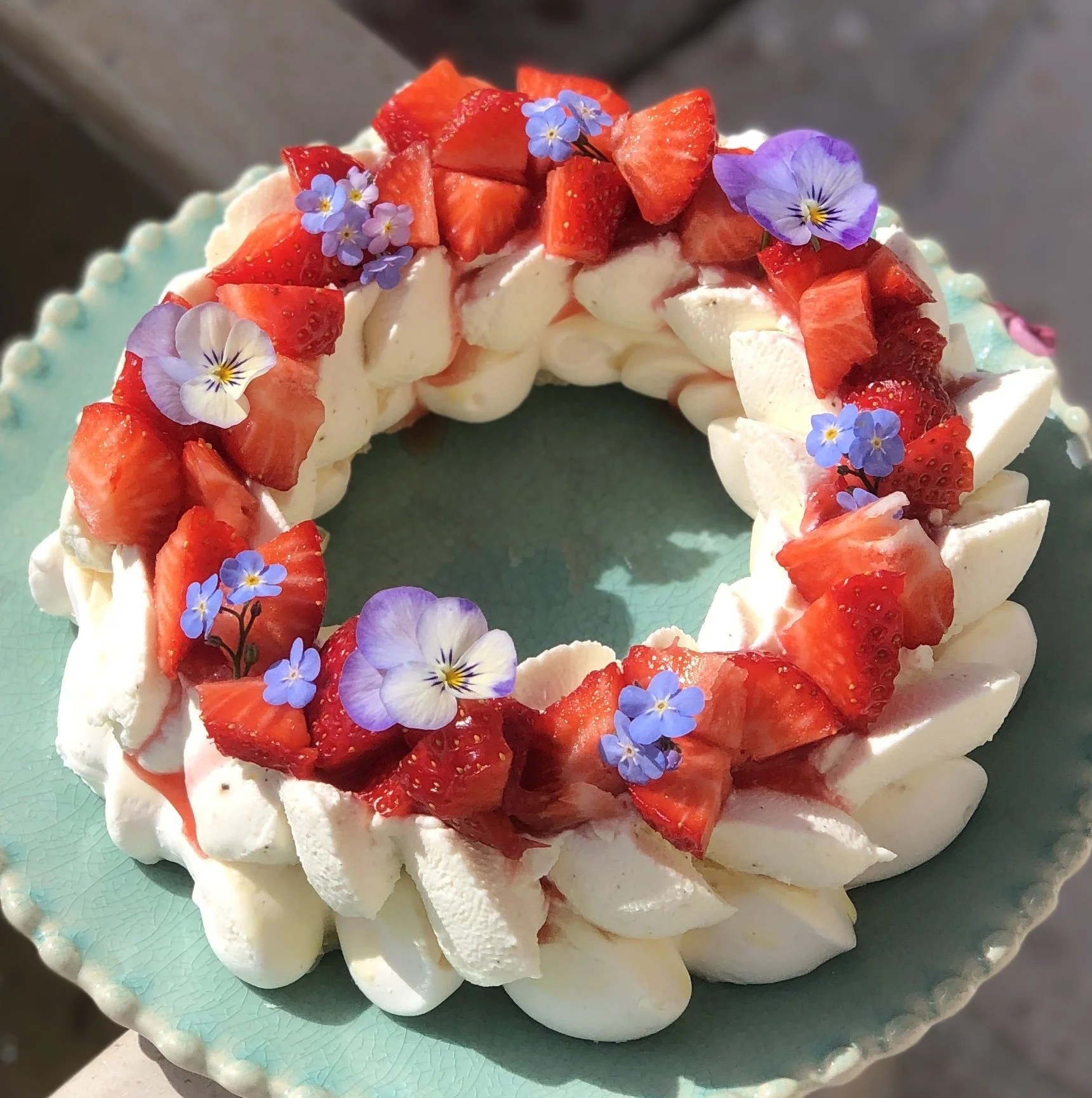 Une pavlova à la fraise décorée de pensée et d'autres fleurs bleues