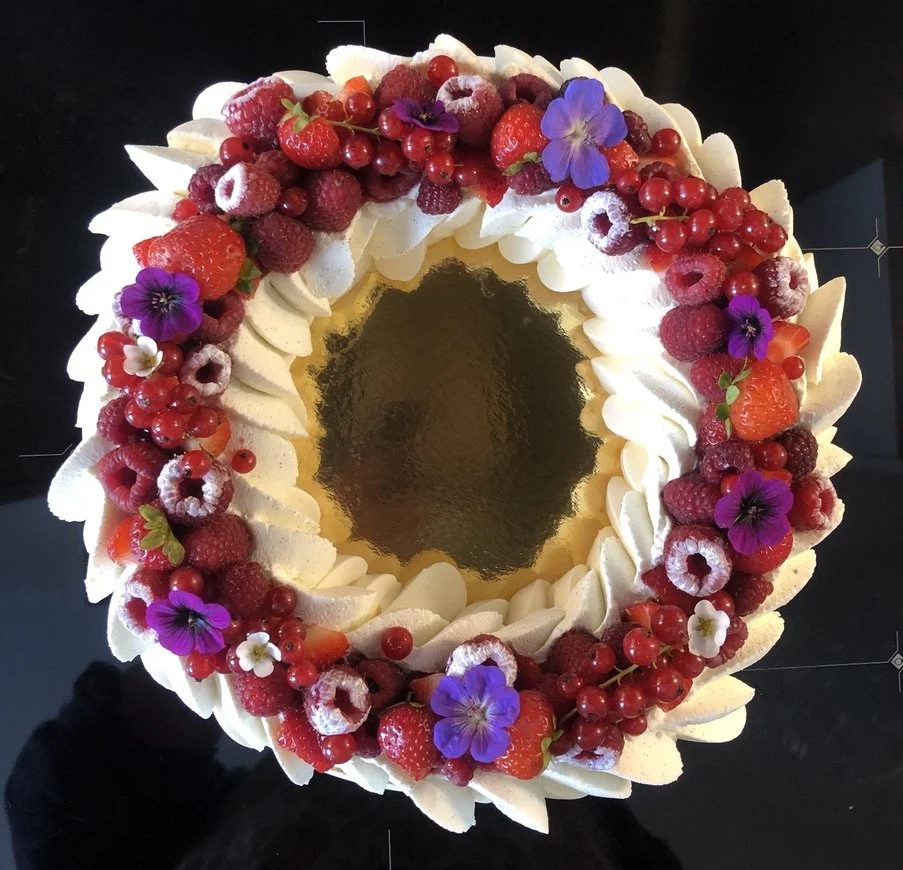 Une pavlova vue du dessus, décoré de framboises, groseilles, fraises et des fleurs blanches et violettes