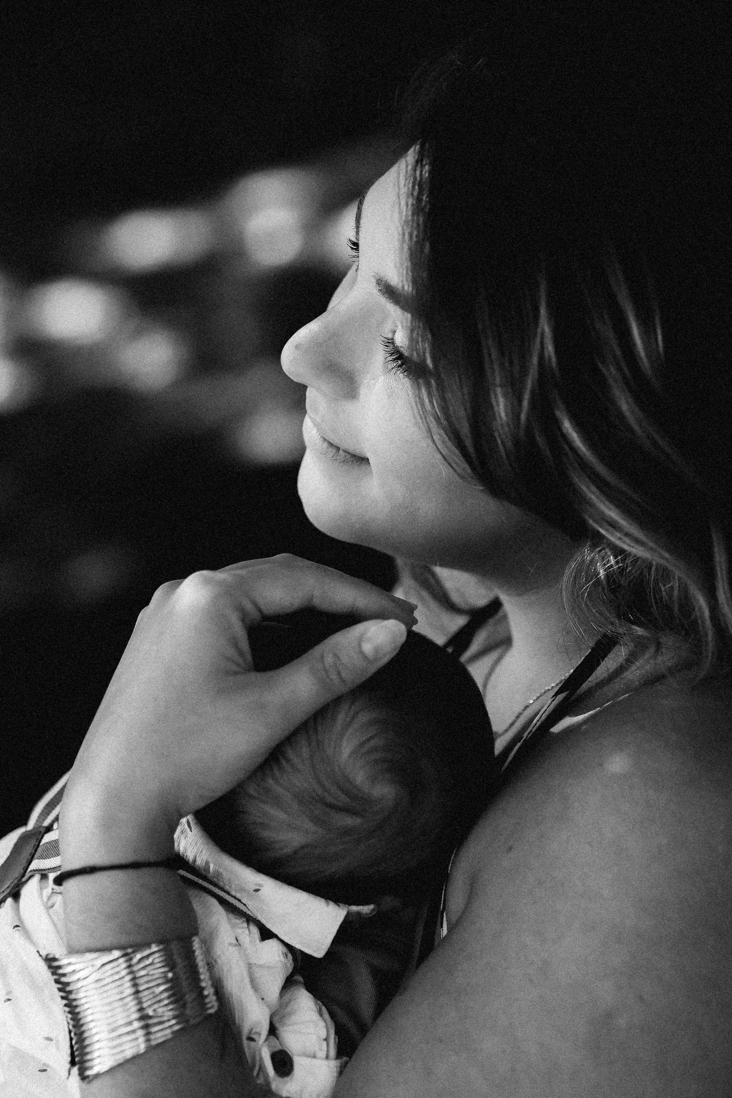 Une femme souriante tient un bébé contre elle, en noir et blanc.