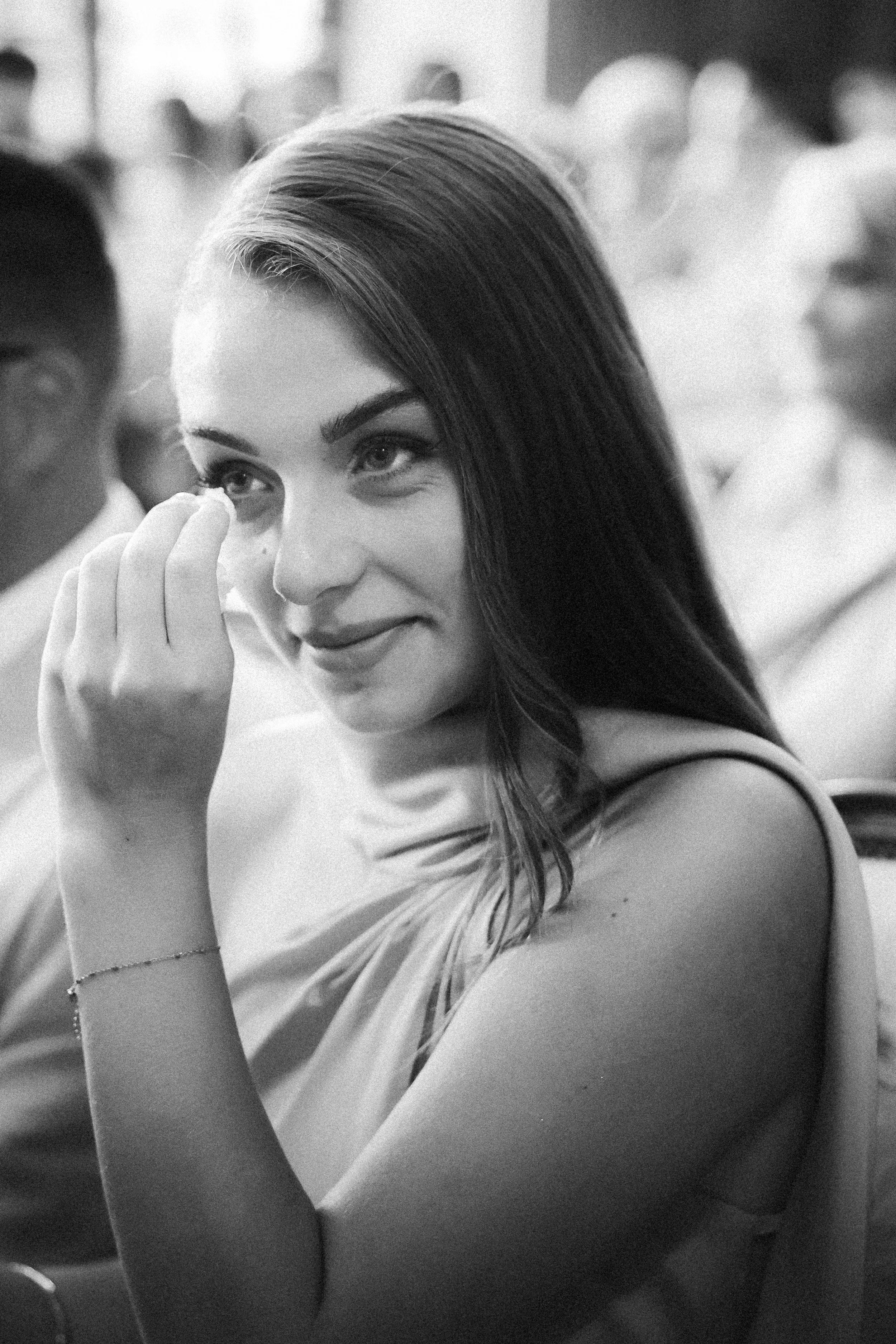 Une jeune femme souriante en dressant légèrement les yeux, touchant son œil avec la main, dans un contexte social ou formel.