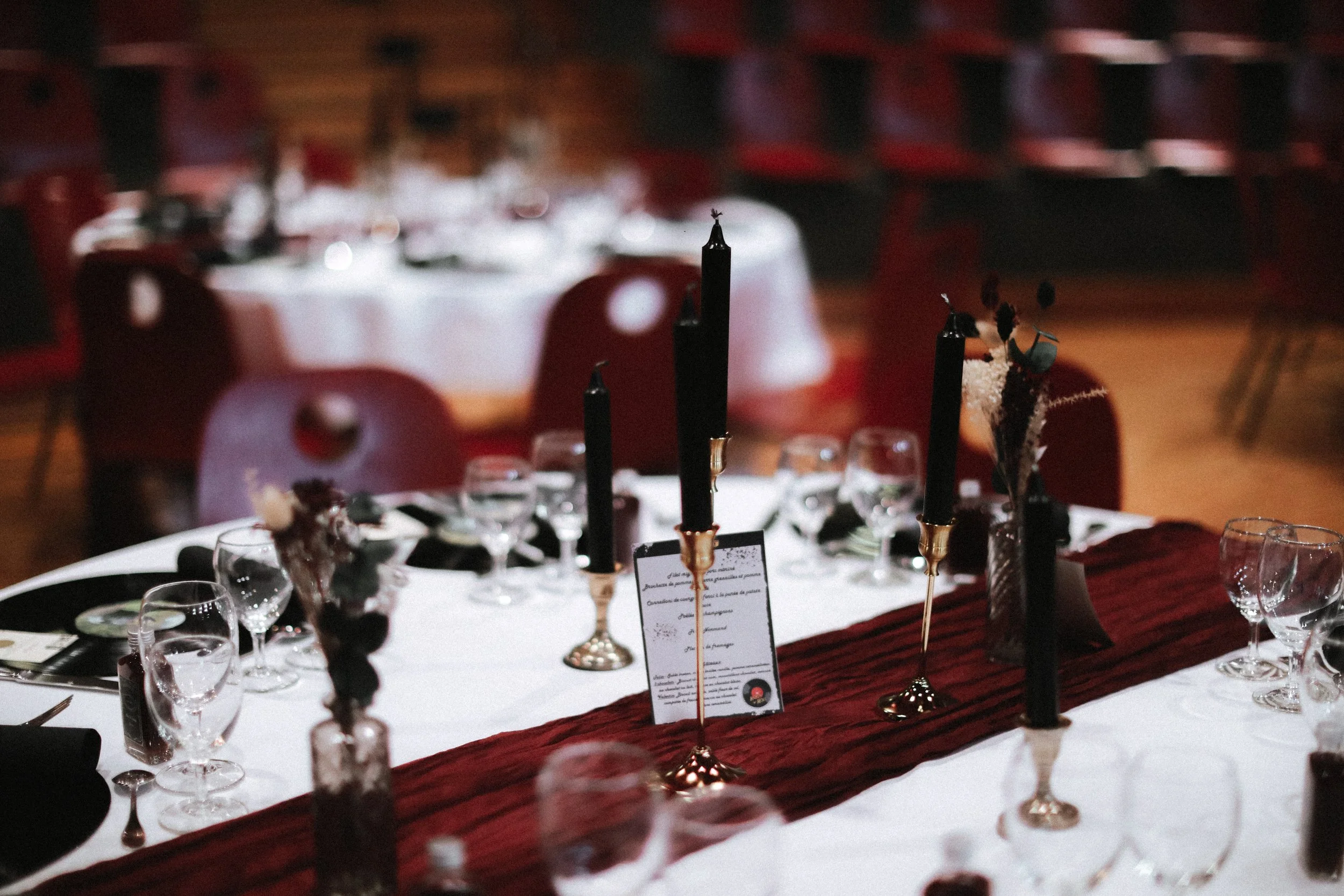Table de fête décorée avec des chandelles noires, fleurs séchées, verres à vin et menu, ambiance chaleureuse et élégante.