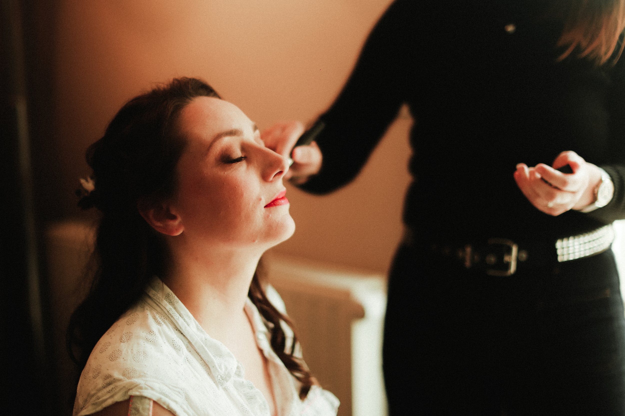 Une femme est en train de se faire maquiller par une autre personne dans un intérieur chaleureux.