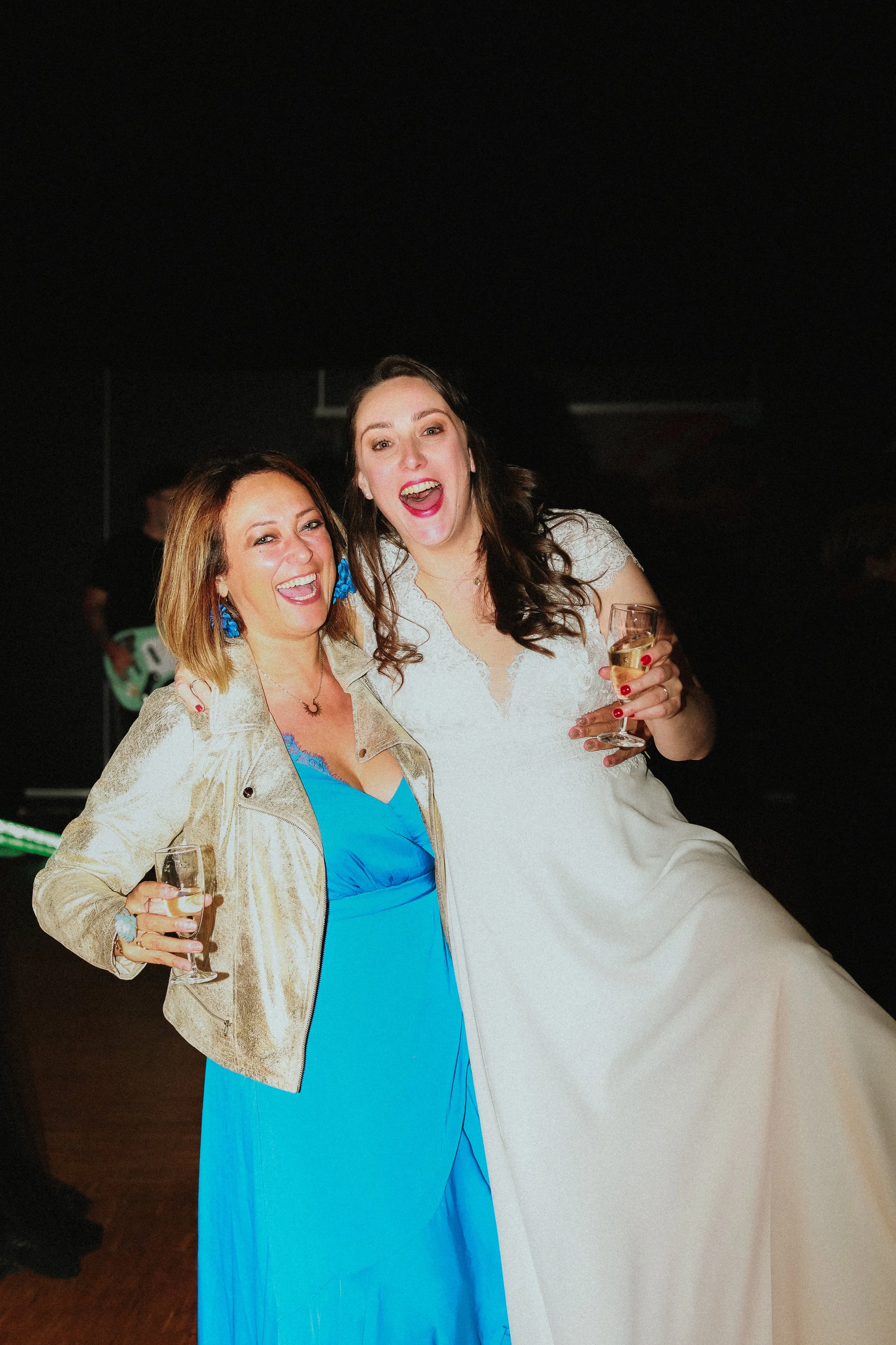 Deux femmes souriantes et habillées élégamment, tenant des verres de champagne, lors d'une fête ou d'un mariage.
