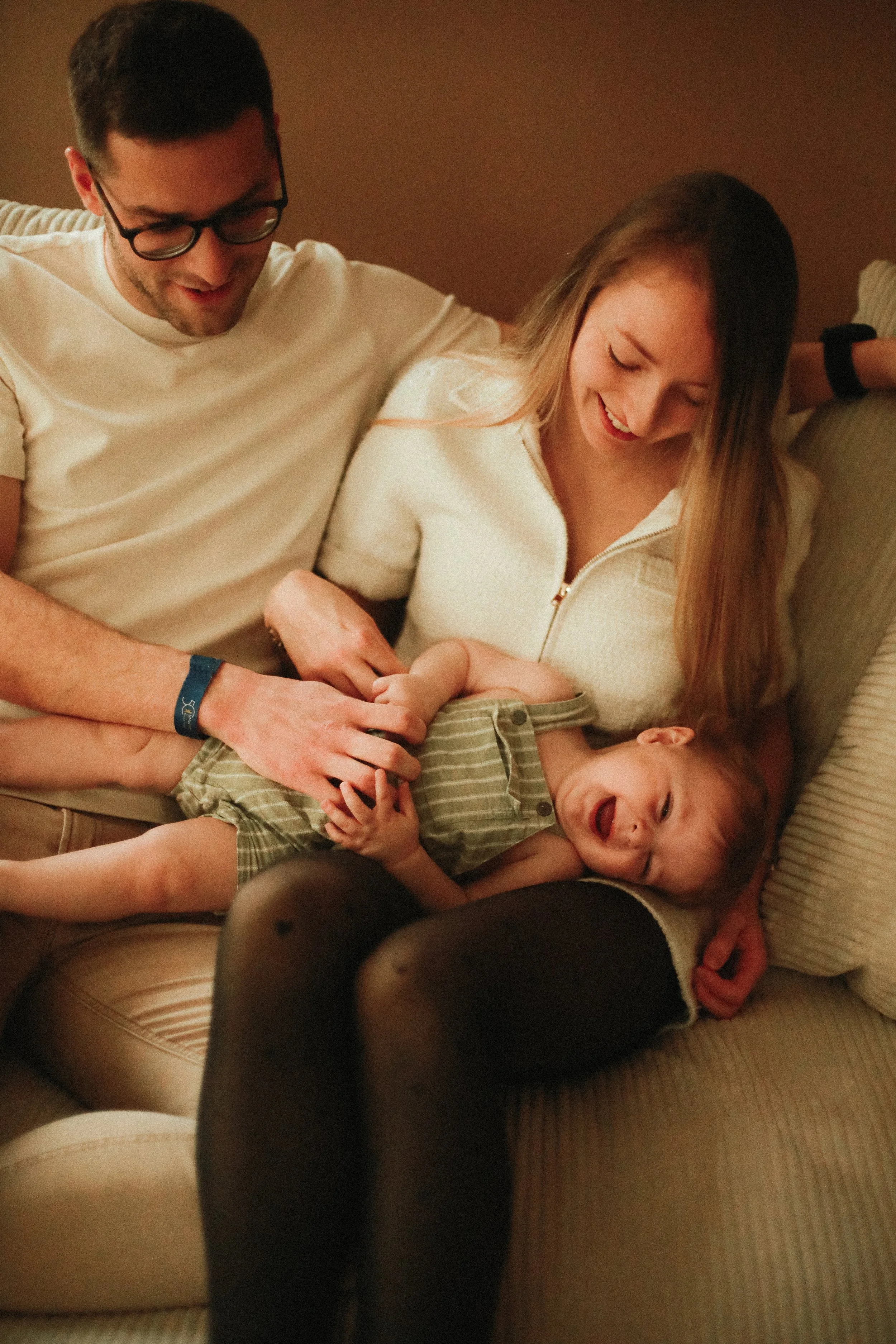 Une famille souriante, composée d'un homme, d'une femme et d'un enfant, assis sur un canapé dans une ambiance chaleureuse.