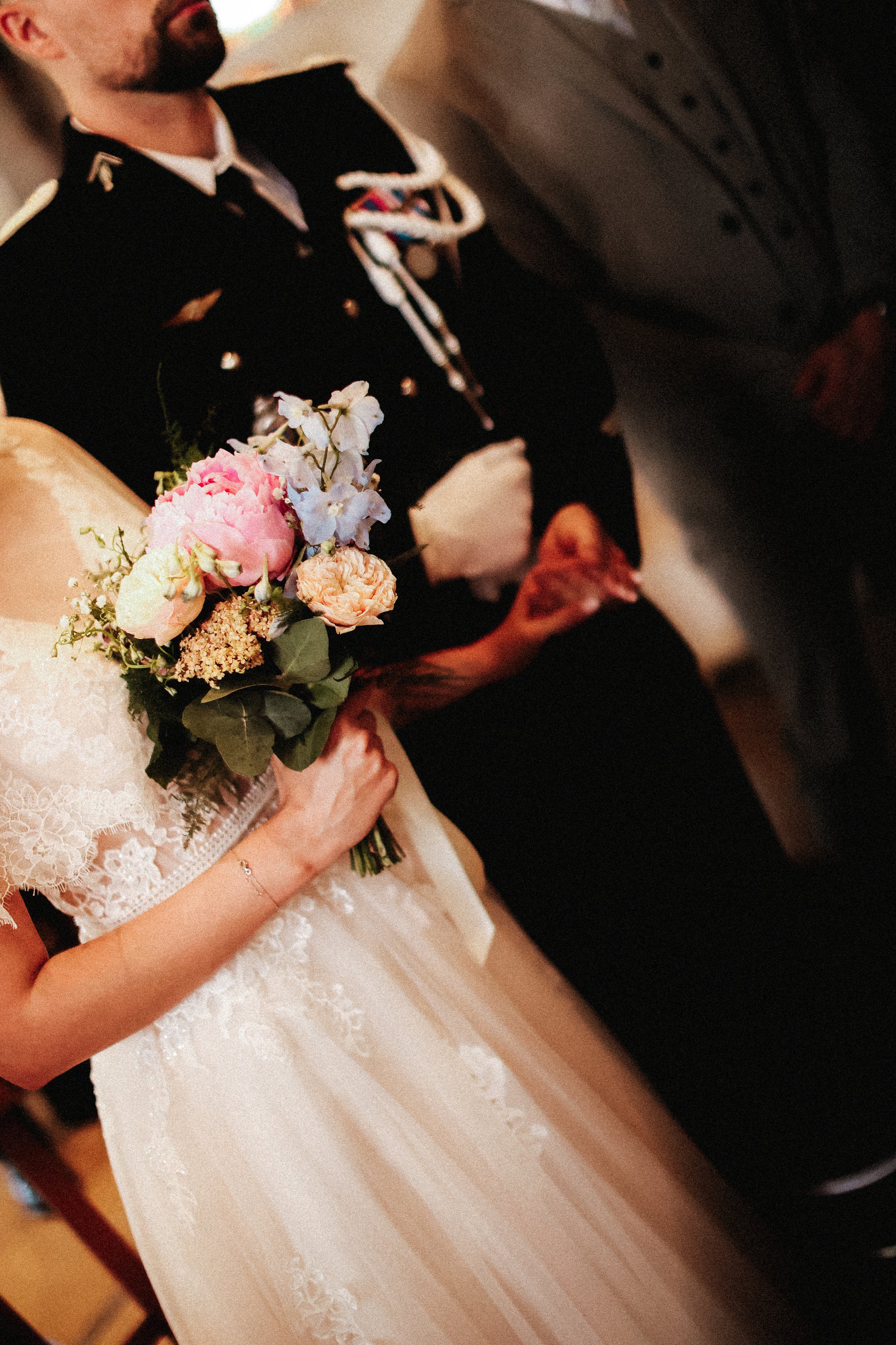 Une mariée tient un bouquet de fleurs pastel, assise à côté d'une personne en uniforme de cérémonie, lors d'un mariage