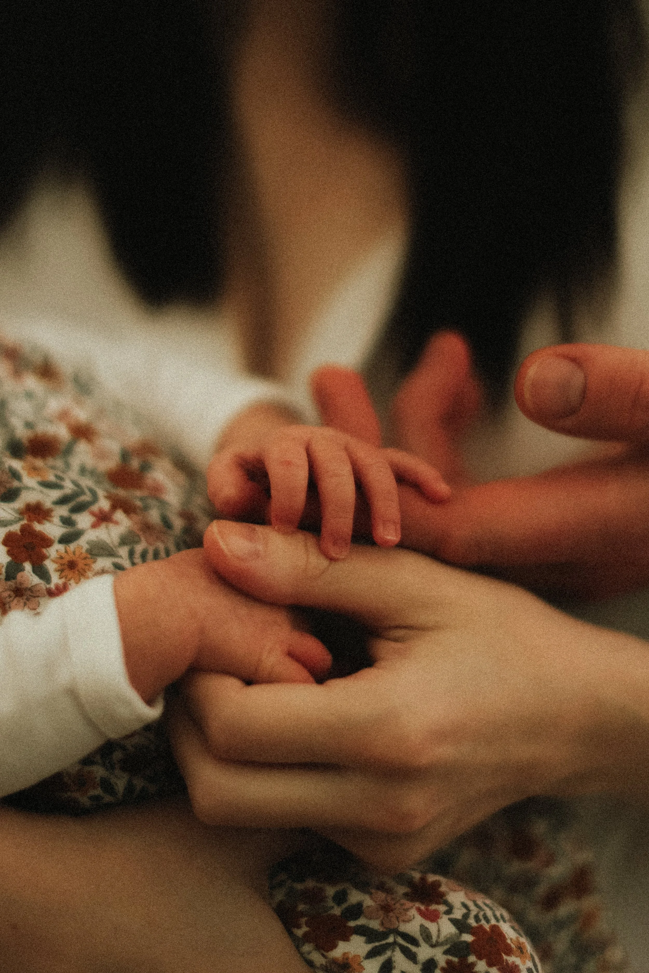 Gros plan sur plusieurs mains : une adulte tenant la main d'un bébé, qui touche la peau de l'adulte avec ses doigts.