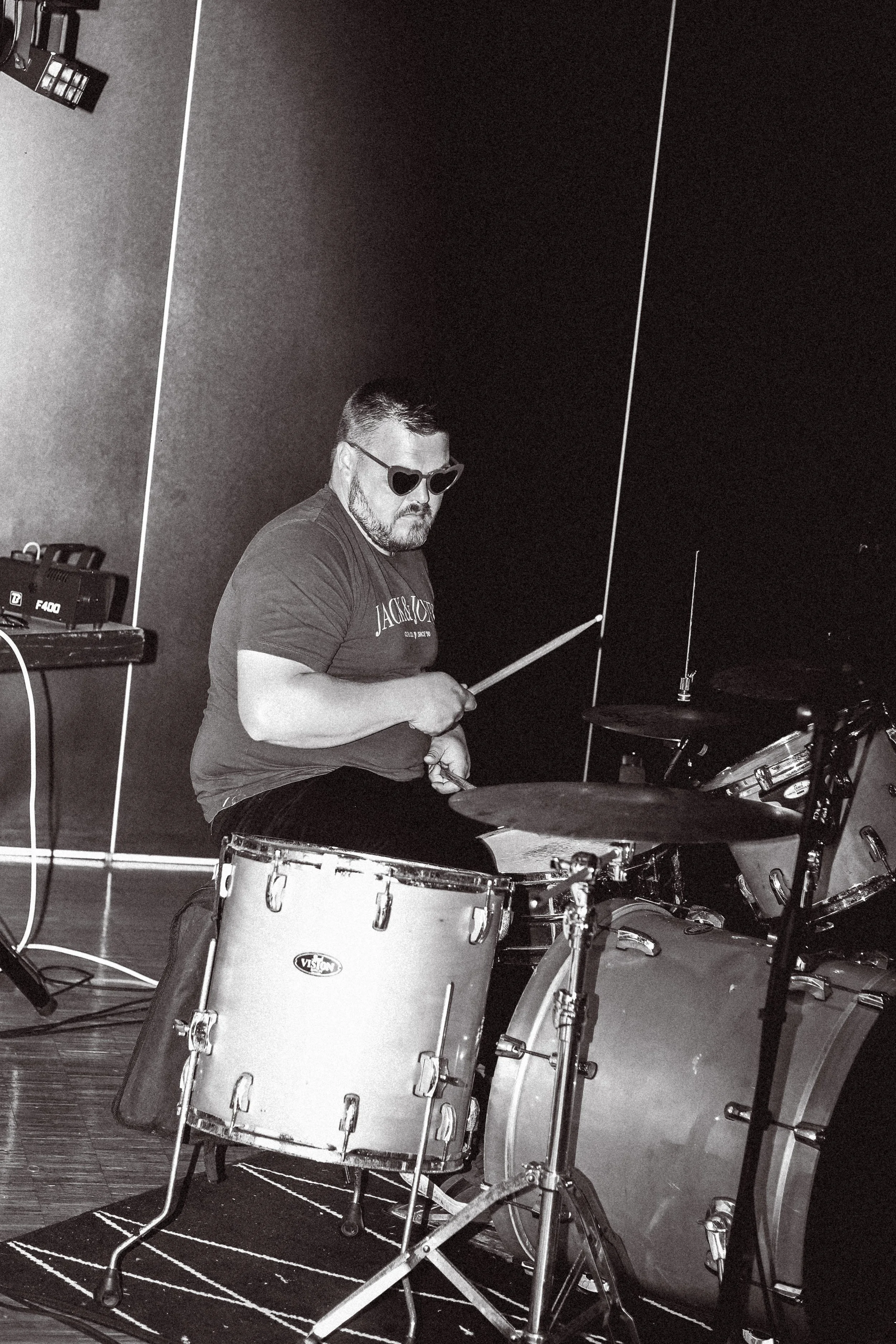 Un homme jouant de la batterie dans une salle de musique, portant des lunettes en forme de cœur.