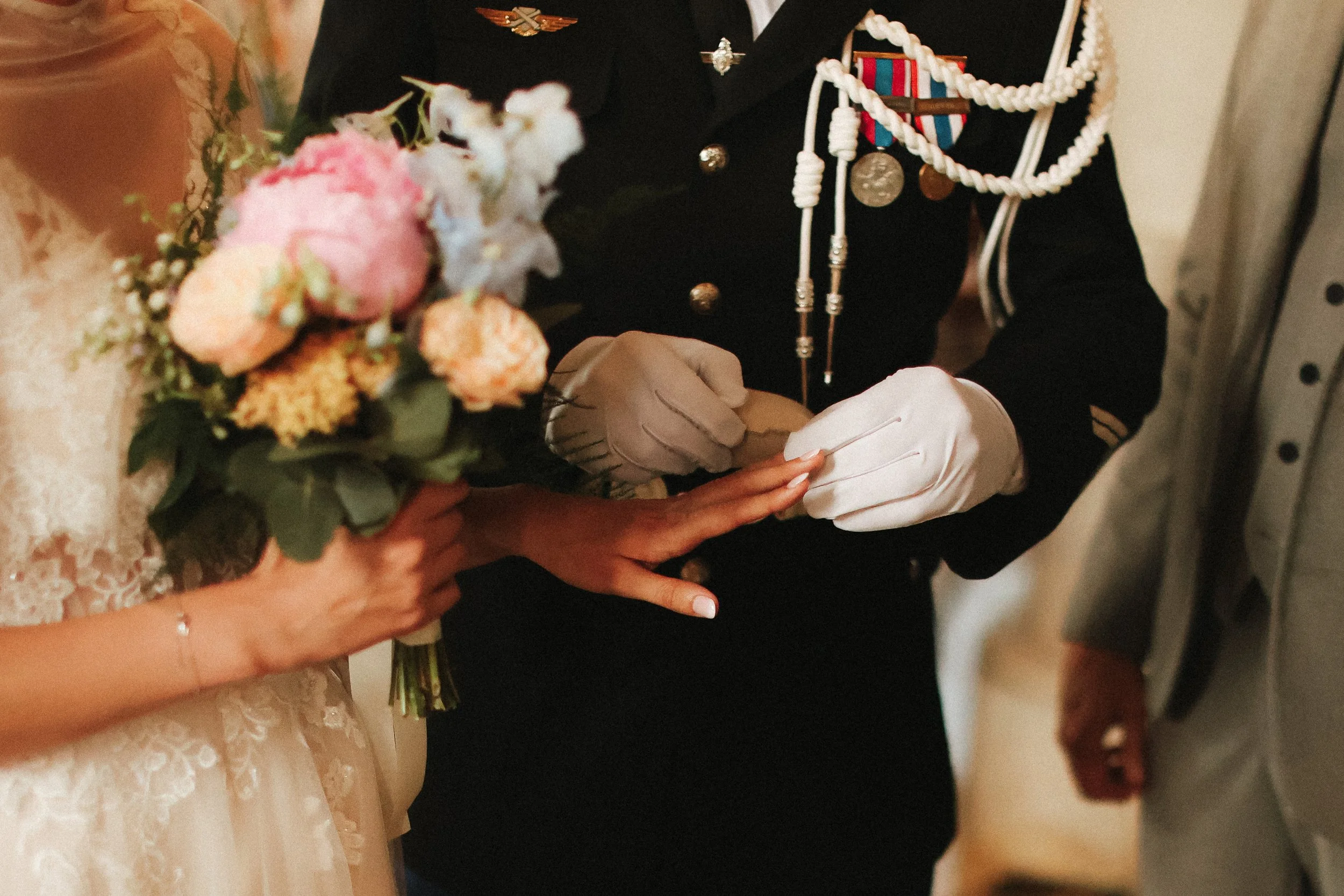 Un officier en uniforme militaire remet un anneau à une femme lors d'une cérémonie de mariage, avec une femme tenant un bouquet de fleurs à proximité.
